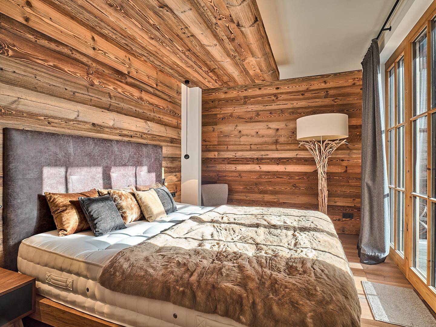 Schlafzimmer im alpinen Stil mit Holzwänden, Holzbalkendecke und Zugang zum Außenbereich.