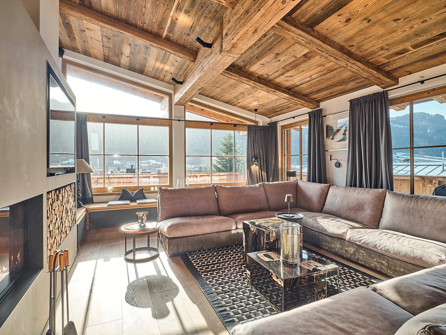 Heller Wohnbereich mit großem Sofa, modernem Kamin und weitem Blick auf die Berge.