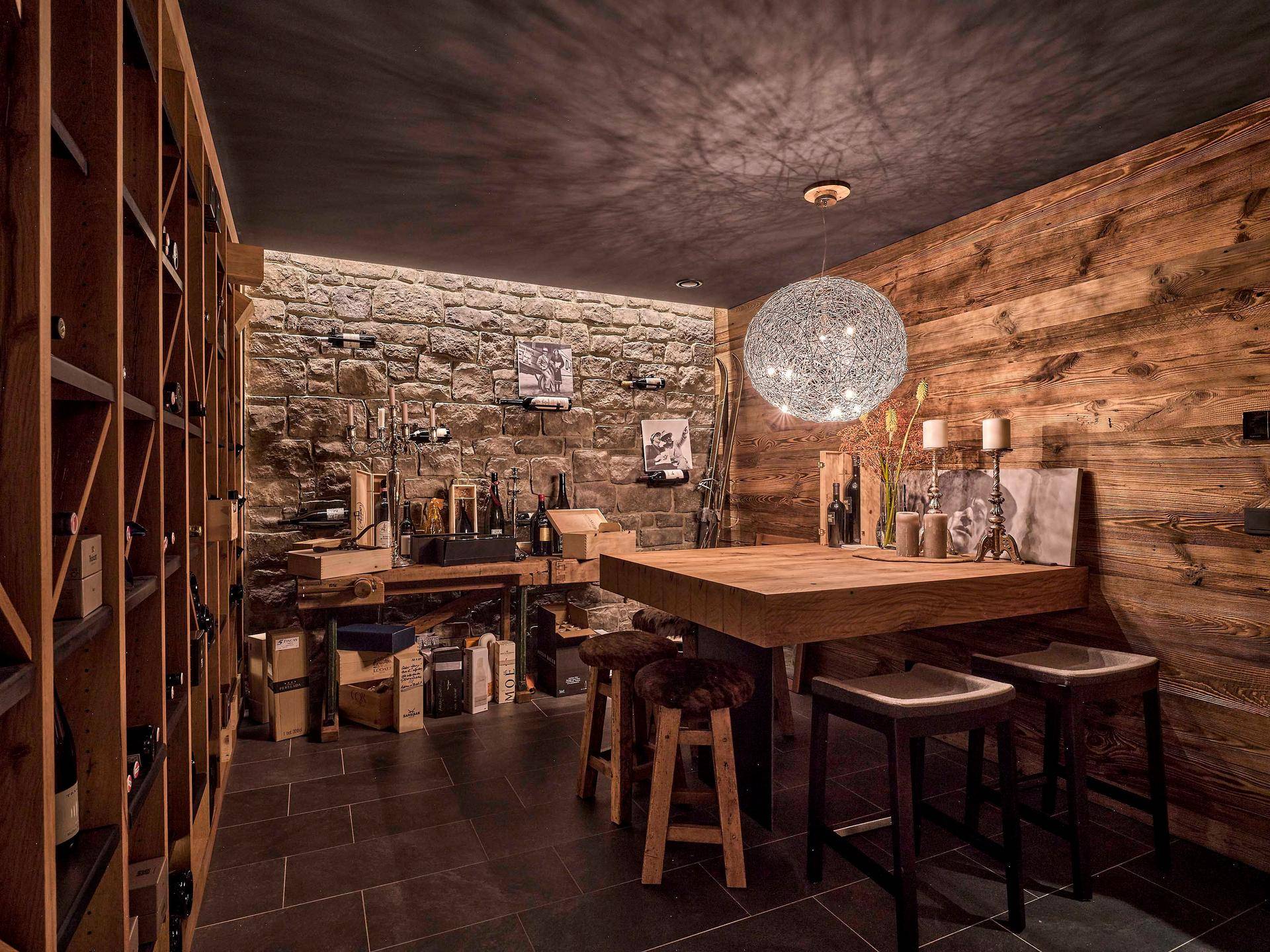 Rustikaler Weinkeller mit Steinwand, Holzregalen und gemütlichem Verkostungsbereich.