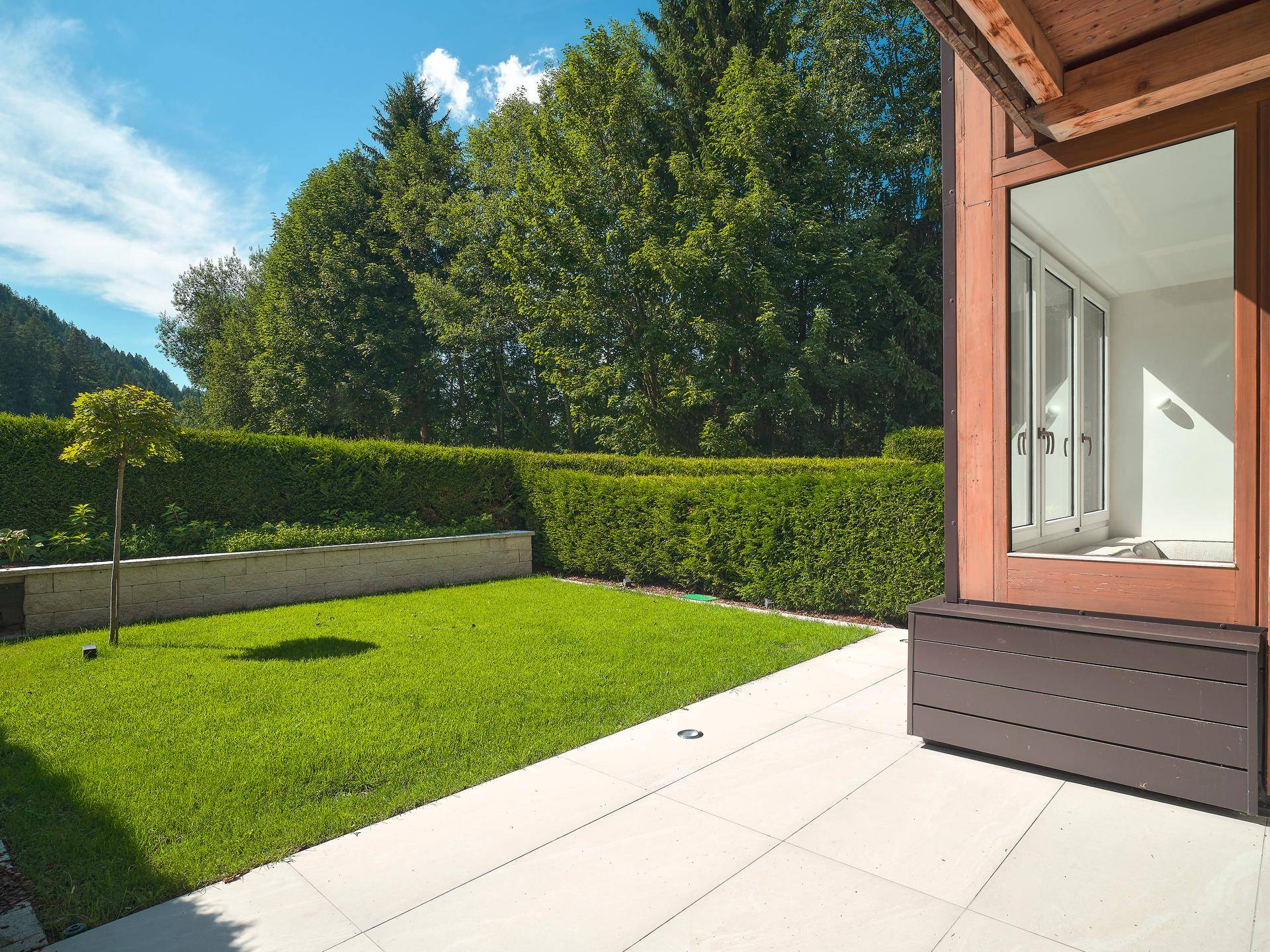 Gepflegter Garten mit Rasenfläche, Terrasse und hoher Hecke für Privatsphäre.