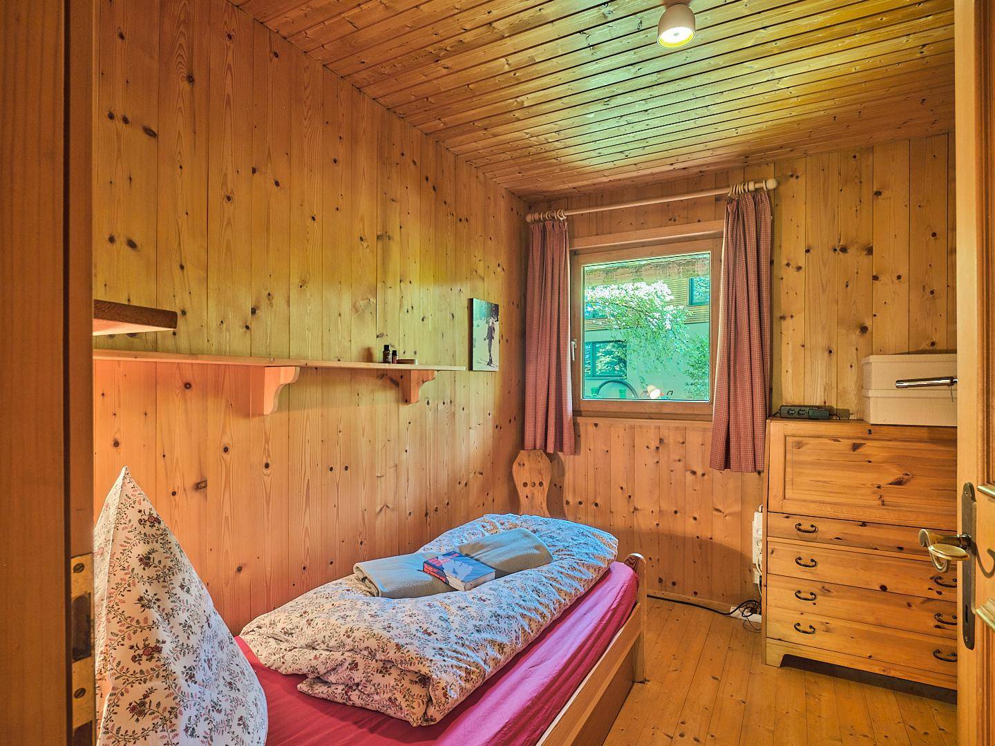 Kleines Schlafzimmer mit Holztäfelung, Einzelbett und rustikalen Holzmöbeln.