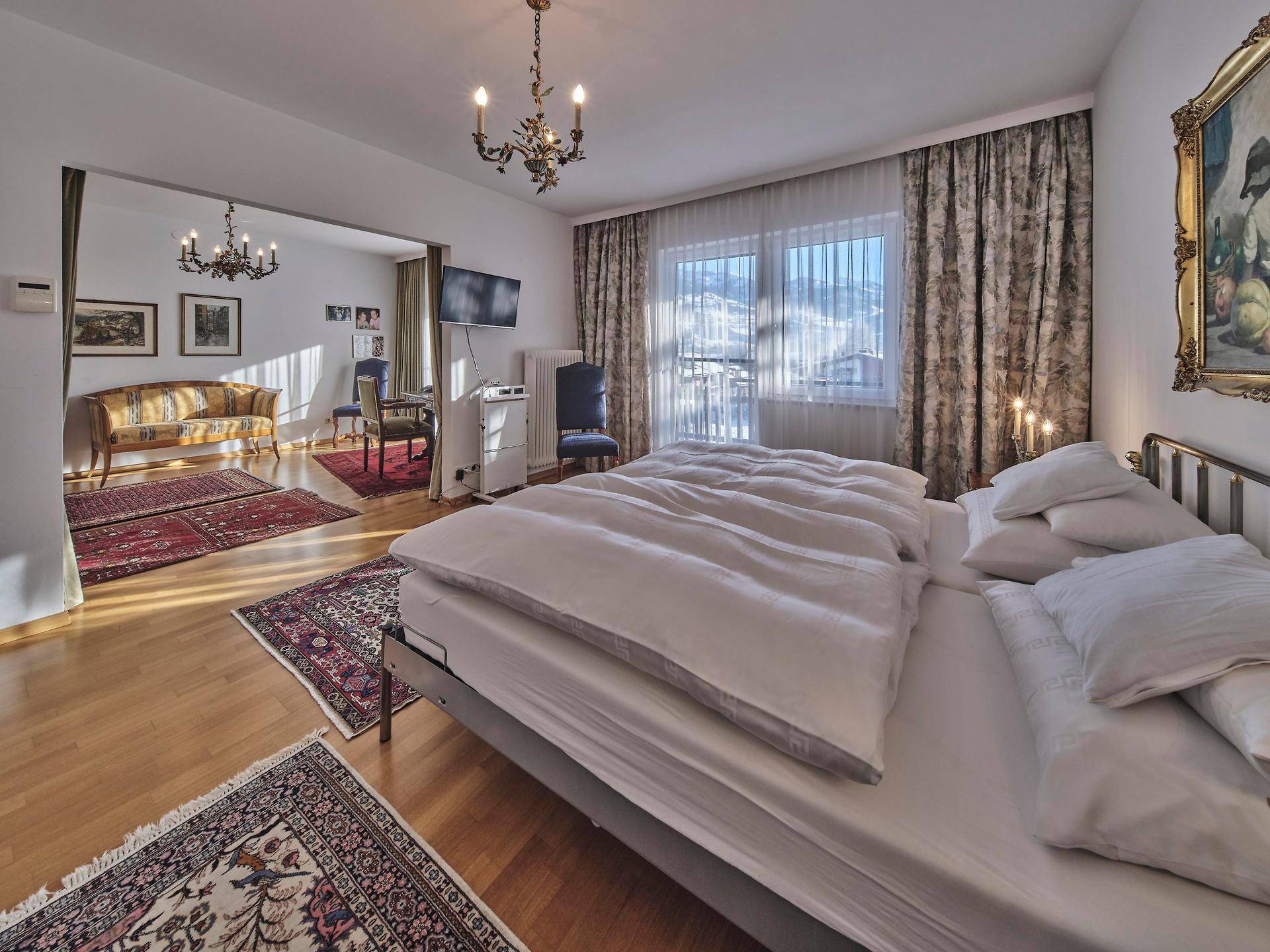 Helles Schlafzimmer mit Holzboden und offenem Übergang zu einem weiteren Wohnbereich mit traditionellen Möbeln.