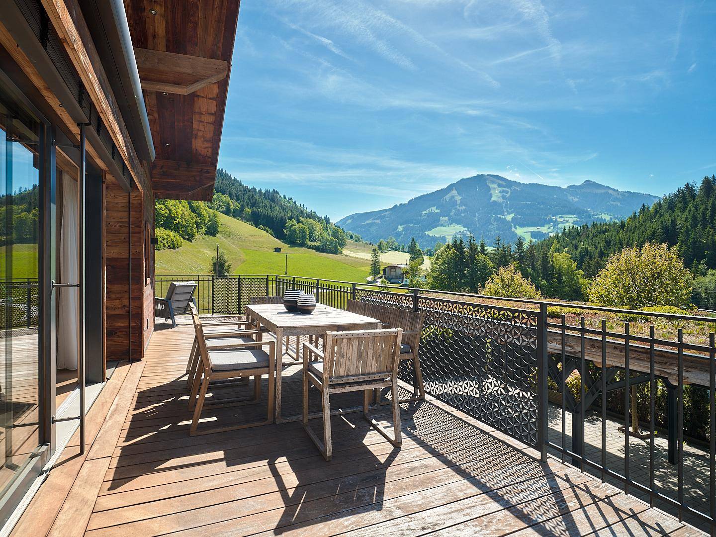 Geräumiger Holzbalkon mit Esstisch und Stühlen, der einen weiten Blick auf die Berglandschaft bietet.