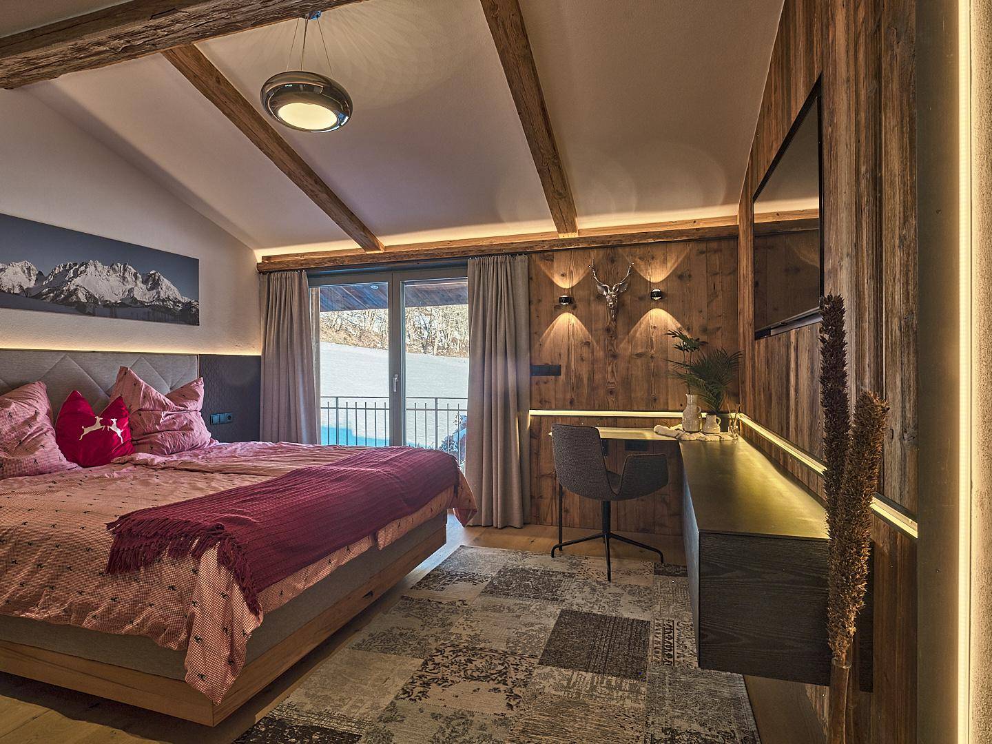 Gemütliches Schlafzimmer mit Holzwänden, sichtbaren Balken und Zugang zu einem Balkon mit Bergblick.