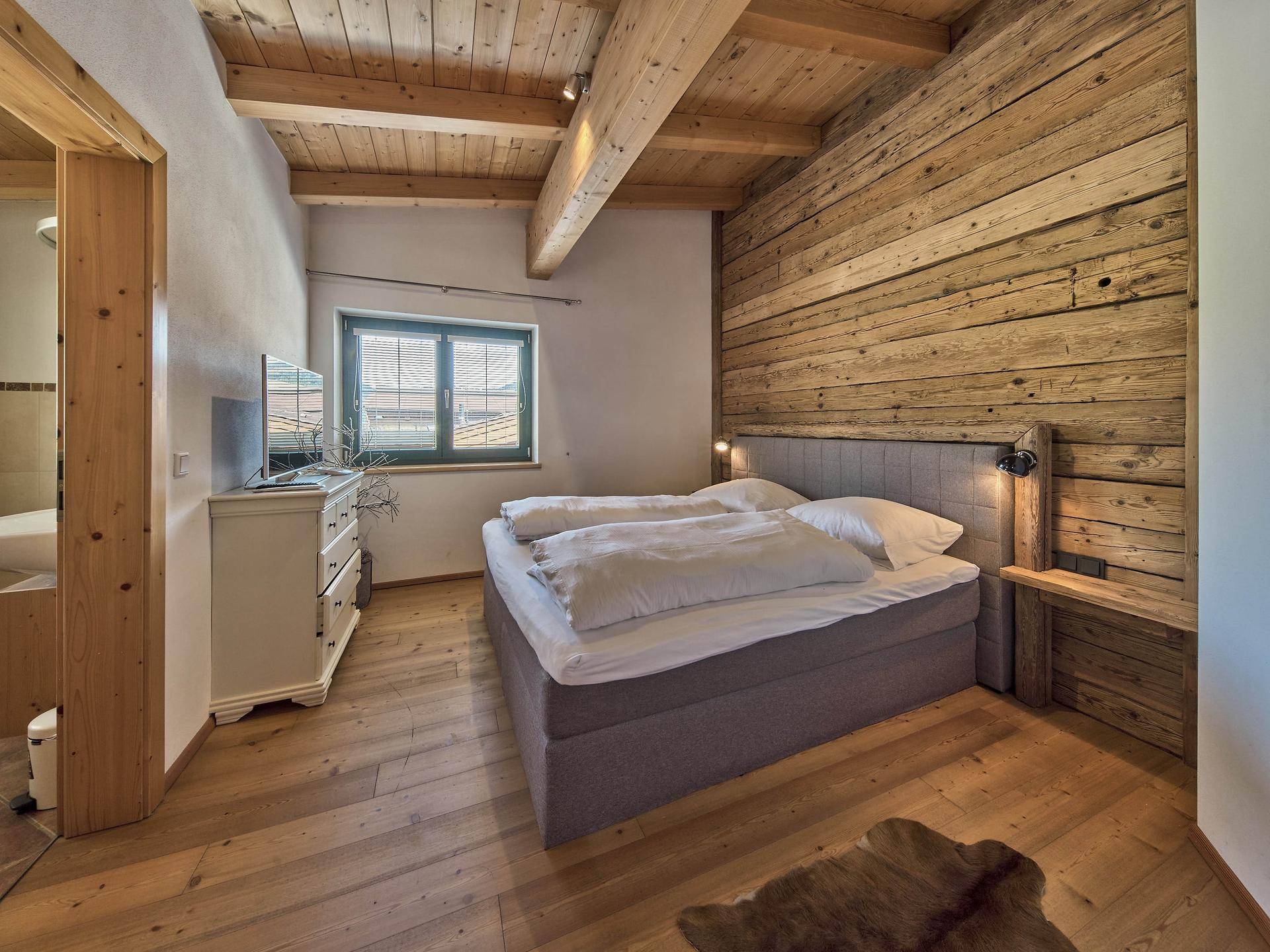 Gemütliches Schlafzimmer im alpinen Stil mit Holzwänden, Holzbalken und einem komfortablen Doppelbett.