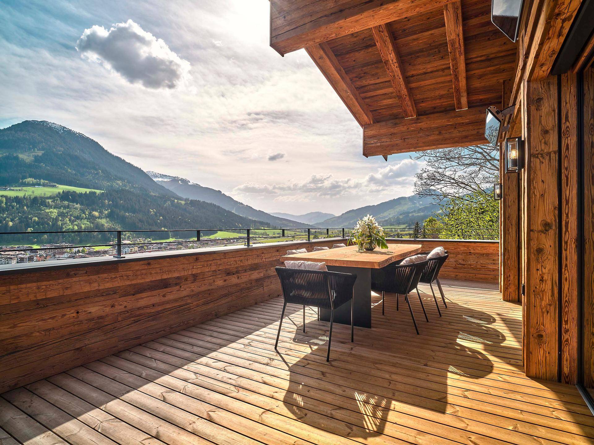 Sonnige Holzterrasse mit Esstisch und Stühlen, ideal für Mahlzeiten im Freien mit Bergblick.