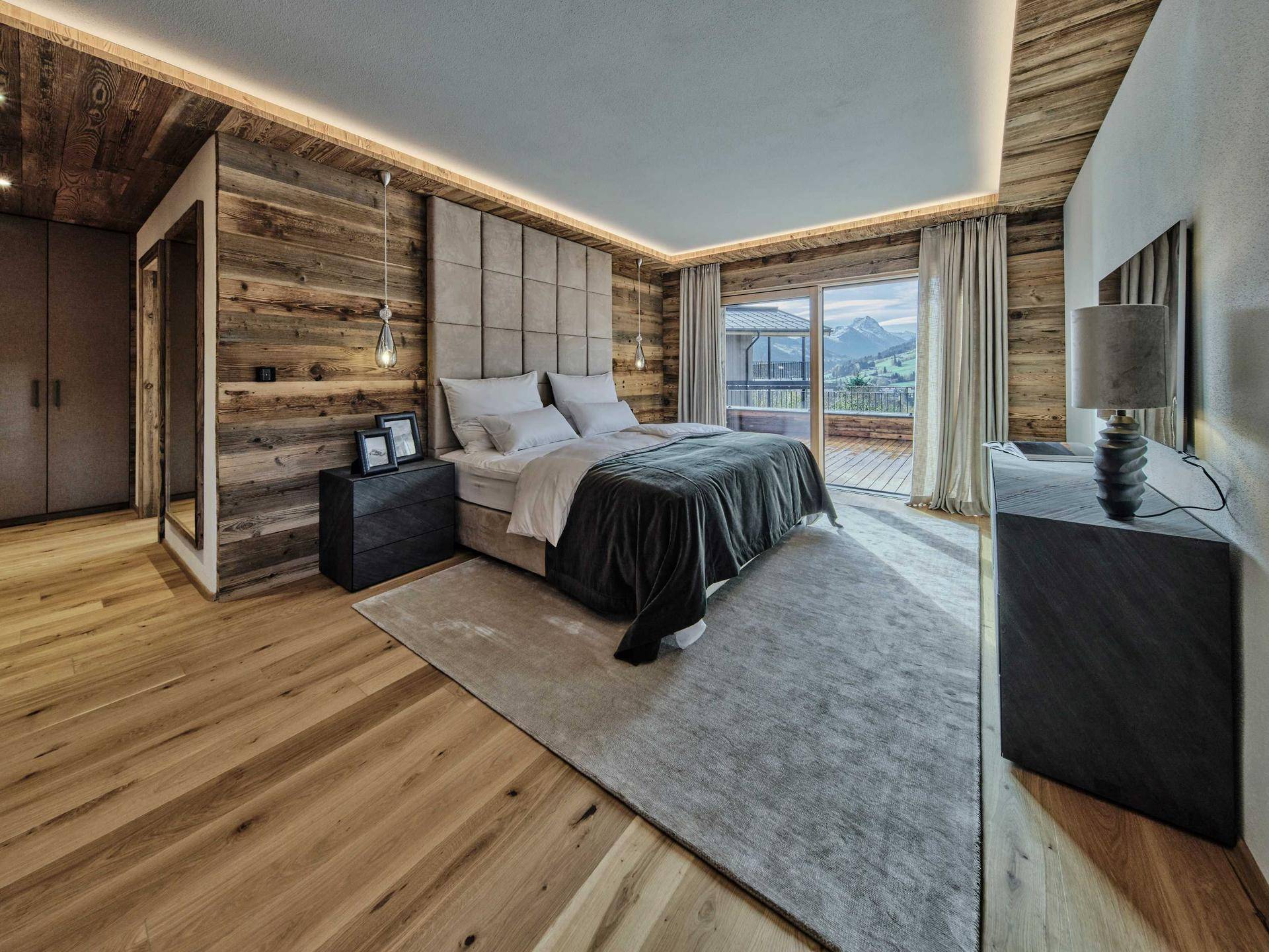 Gemütliches Schlafzimmer mit Holzwänden, indirekter Beleuchtung und Zugang zum Balkon mit Bergblick.