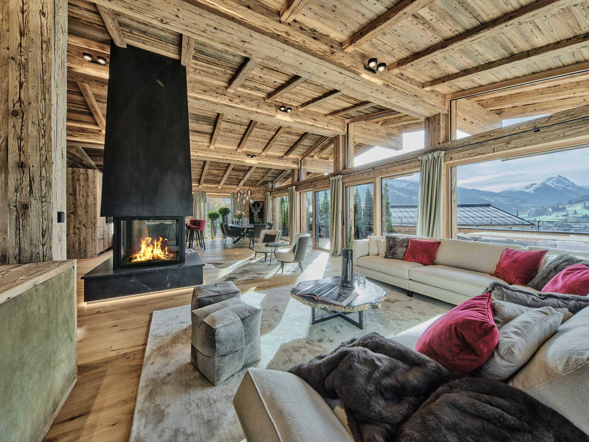 Helles Wohnzimmer mit modernem Kamin, großen Fensterfronten und atemberaubendem Bergblick.