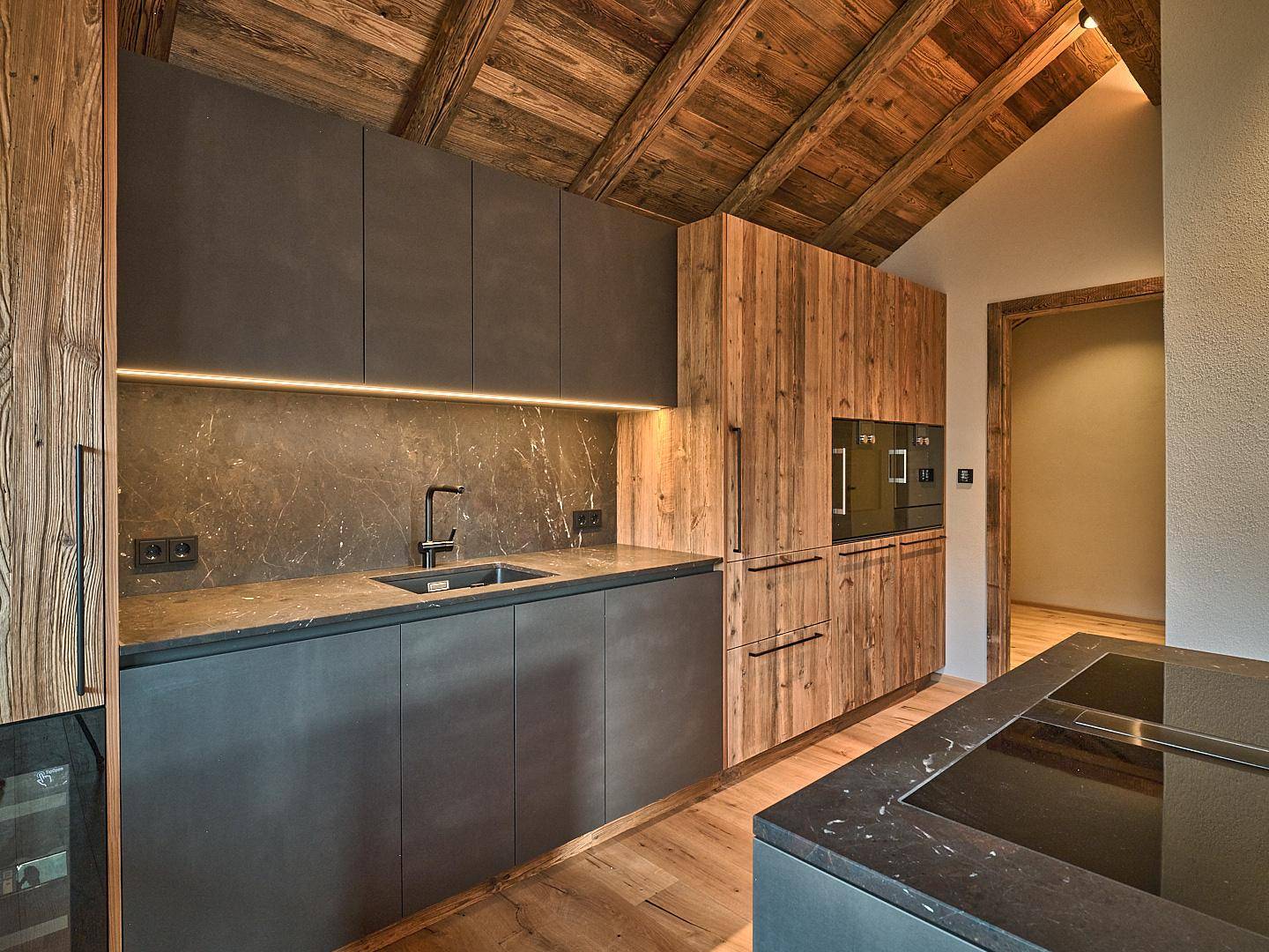 Moderne Küche mit dunklen Fronten, Holzelementen und integrierten Premium-Geräten.