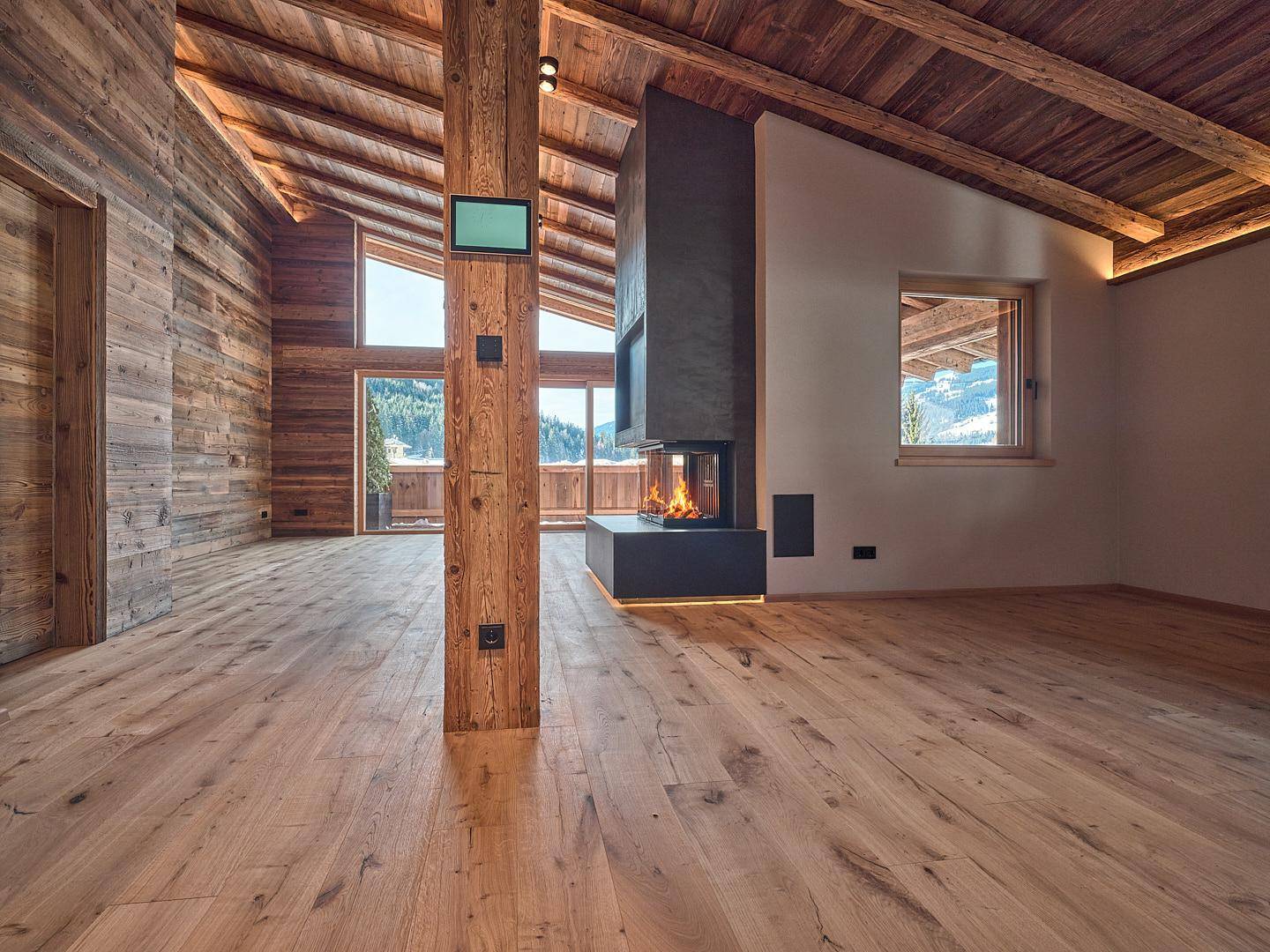 Gemütliches Wohnzimmer mit Holzwänden, Kamin und Blick auf die verschneite Berglandschaft.
