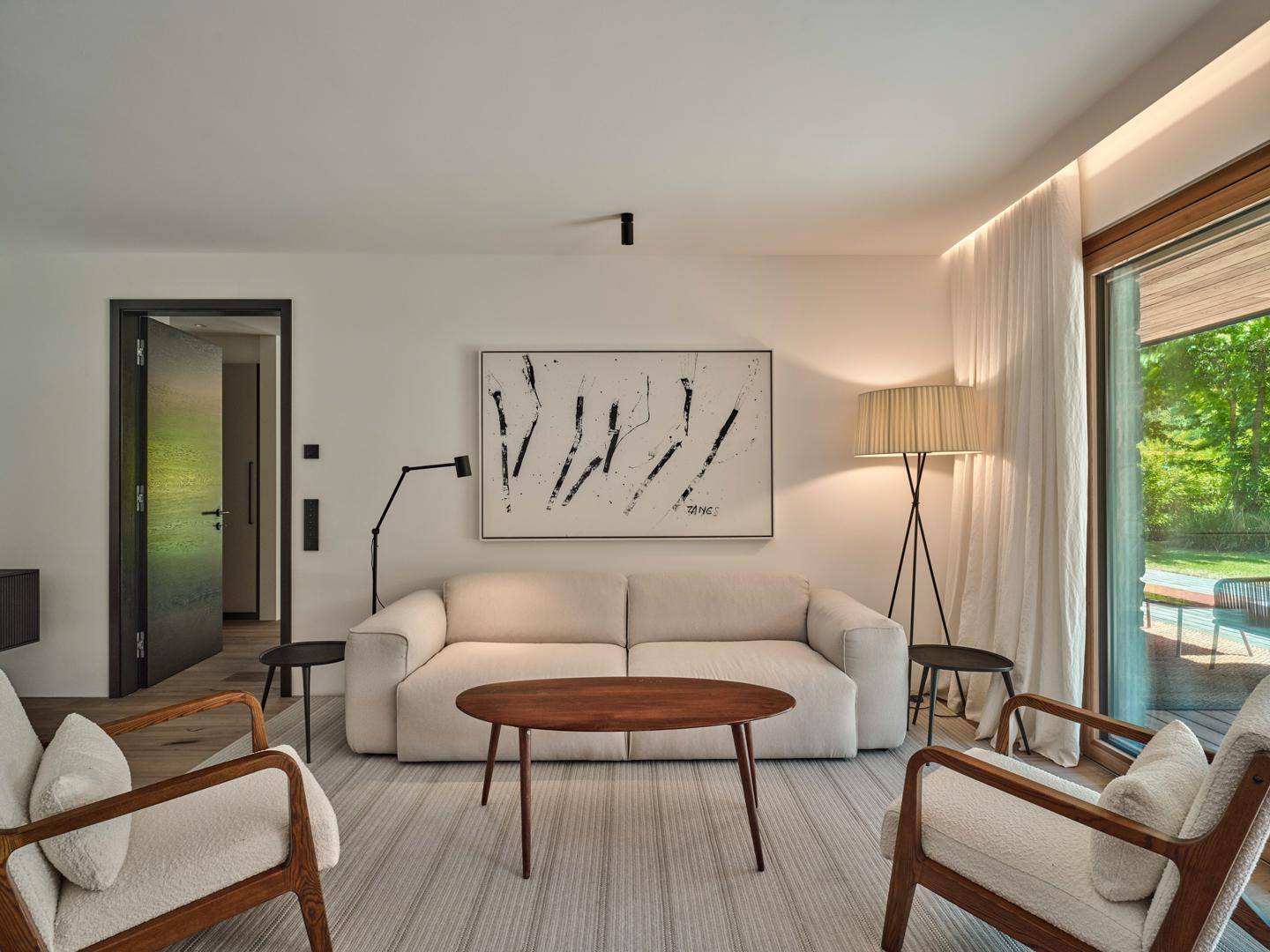 Gemütliches Wohnzimmer mit hellem Sofa, Holztisch und großem Fenster mit Blick ins Grüne.