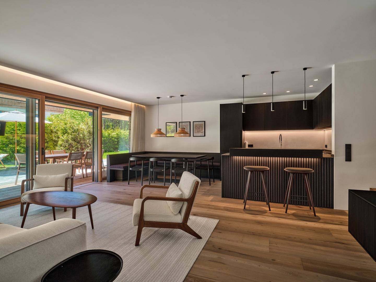 Offener Wohn-Essbereich mit moderner schwarzer Küche, Holzboden und Zugang zur Terrasse.