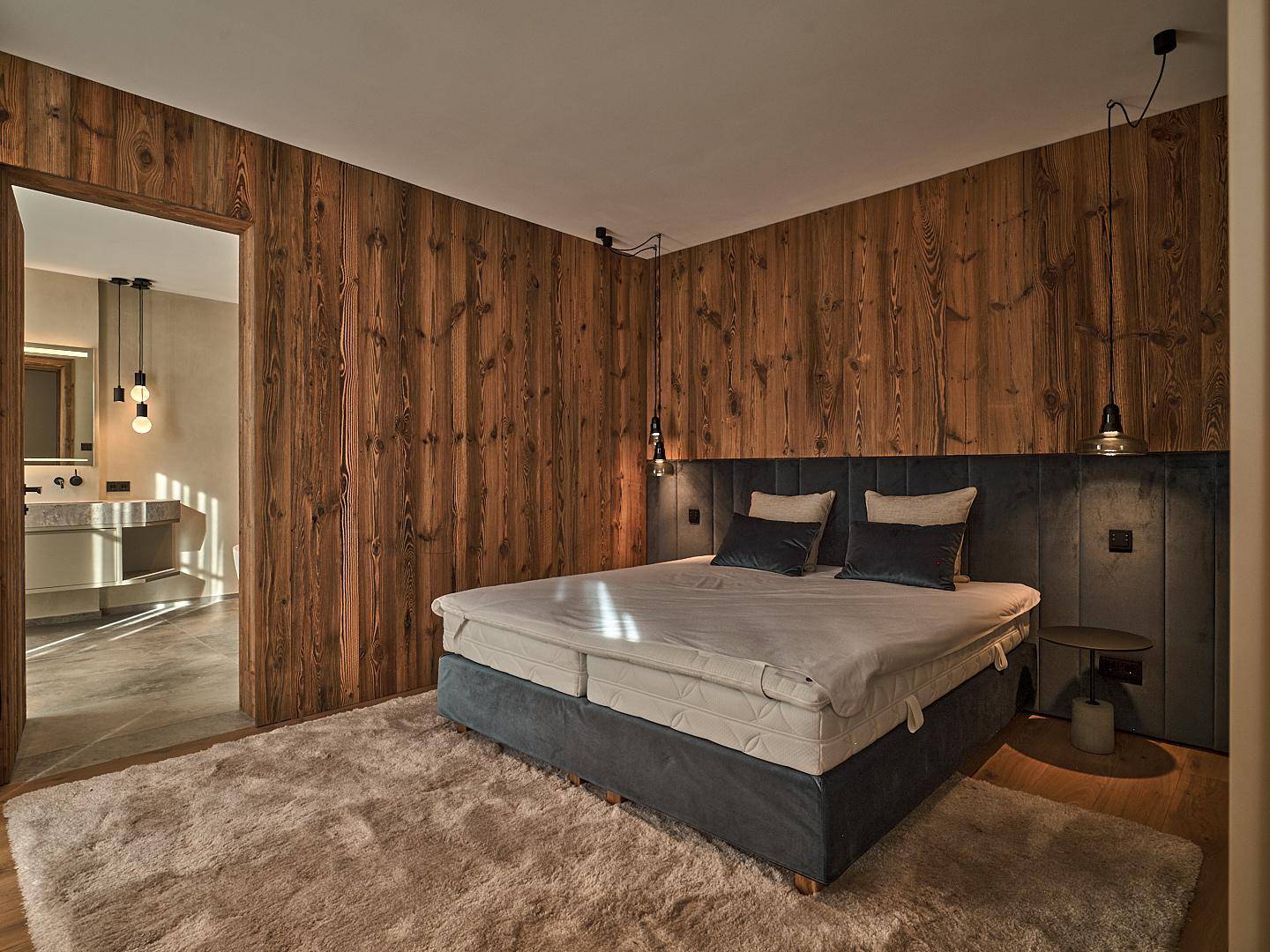 Gemütliches Schlafzimmer mit Holzwänden, großem Doppelbett und direktem Zugang zum luxuriösen Badezimmer.