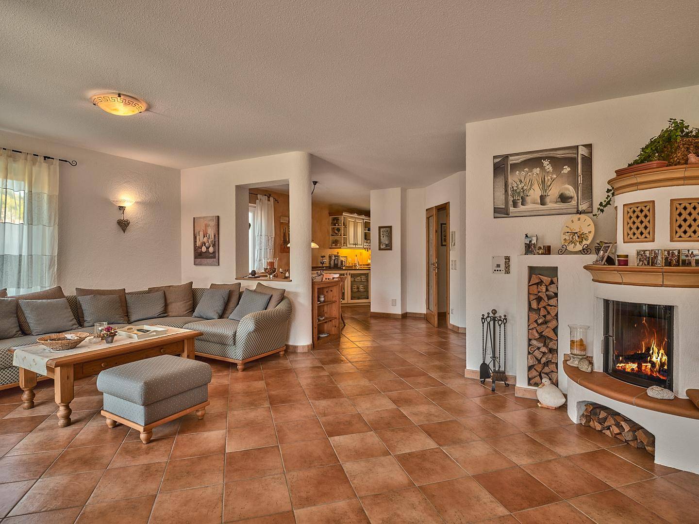 Gemütliches Wohnzimmer mit traditionellem Kachelofen, bequemer Sofalandschaft und Terrakotta-Fliesenboden.