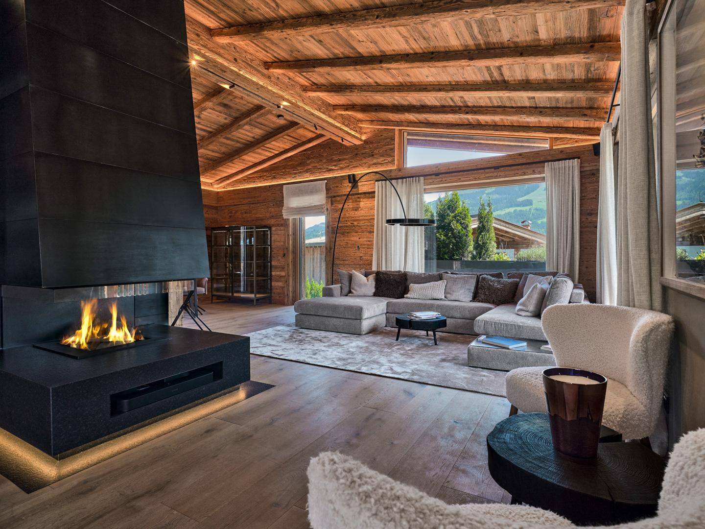 Modernes Wohnzimmer im Chalet-Stil mit großem Kamin, Holzbalkendecke und Panoramablick auf die Berge.