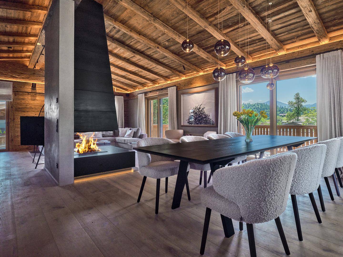 Eleganter offener Wohn- und Essbereich mit Holzbalkendecke, modernem Kamin und Bergblick.