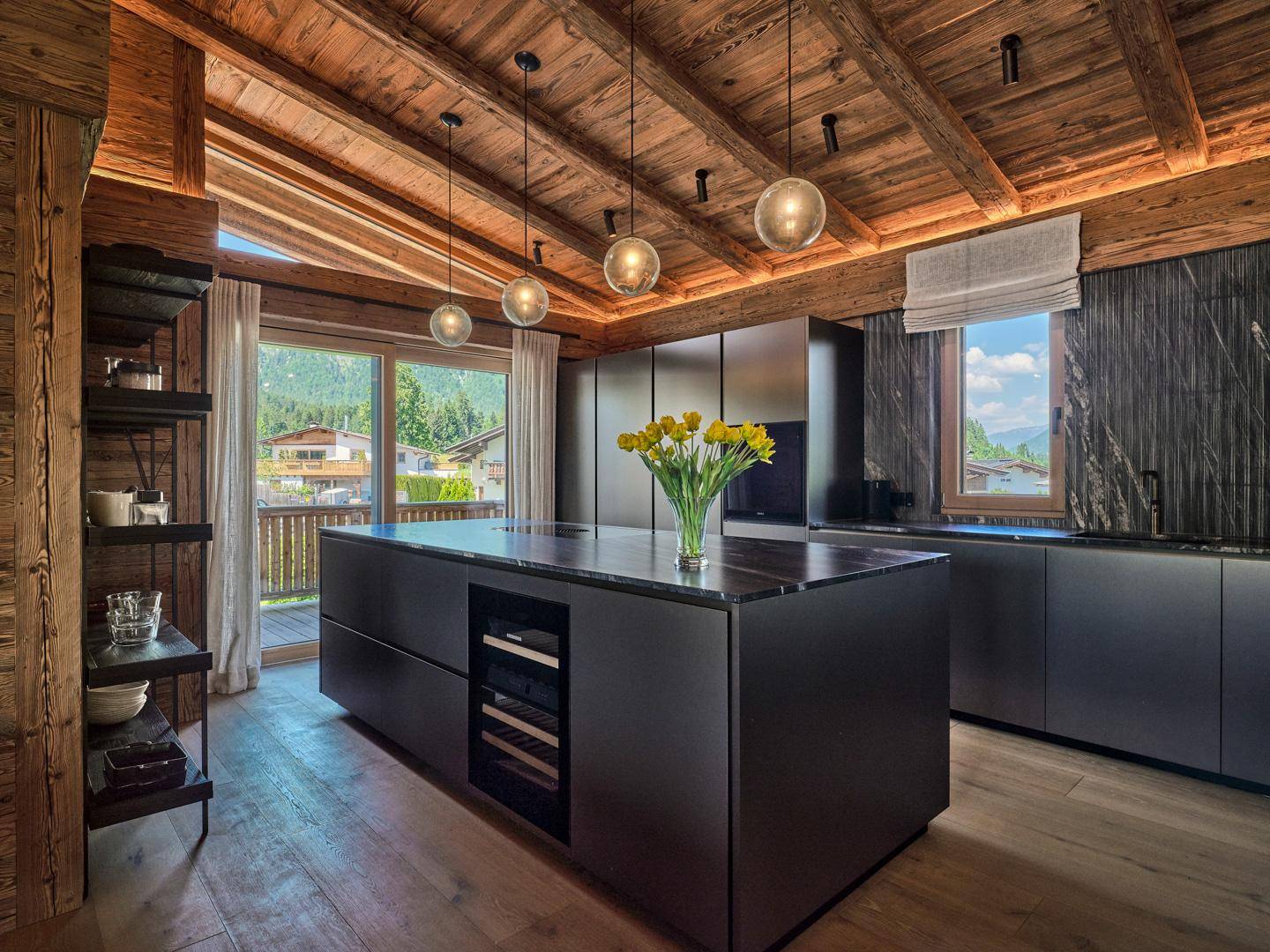 Moderne schwarze Küche mit großer Kochinsel, Holzbalkendecke und Zugang zum Balkon.