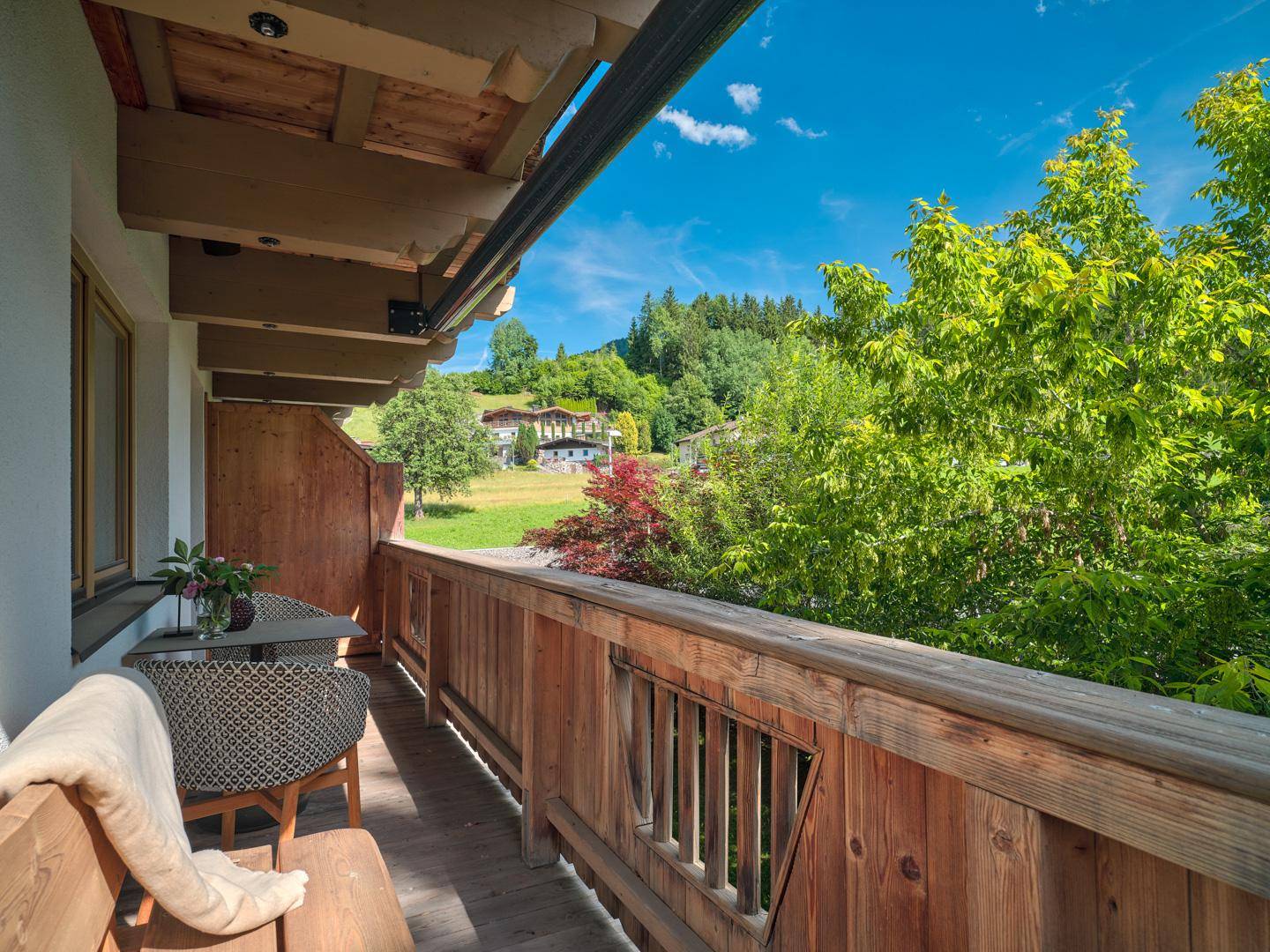 Geräumiger Balkon mit Holzboden, Sitzgelegenheiten und weitem Blick auf die grüne Landschaft.