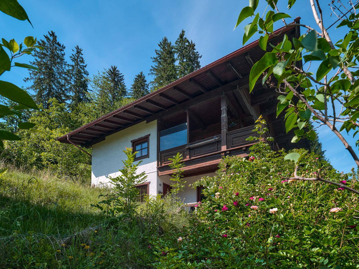 Seitenansicht des Hauses mit traditionellem Holzbalkon und üppiger Vegetation im Vordergrund.