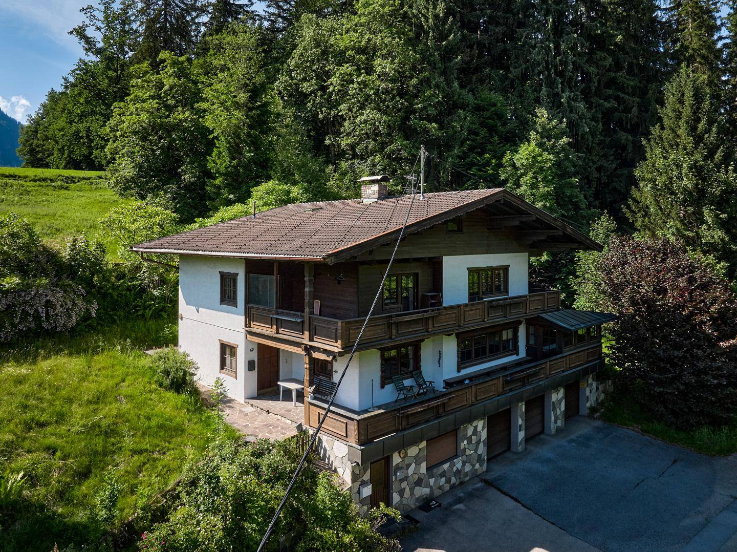 Alpines Wohnhaus mit mehreren Holzbalkonen, Steinsockel und umgeben von grüner Natur.