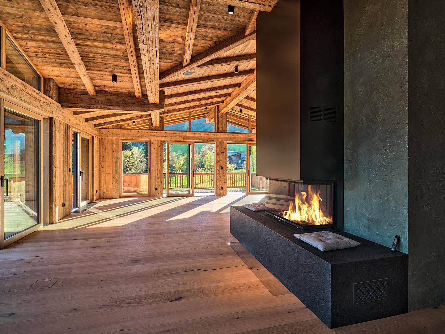 Lichtdurchflutetes Wohnzimmer im Chalet-Stil mit Holzbalken, Kamin und Bergblick.