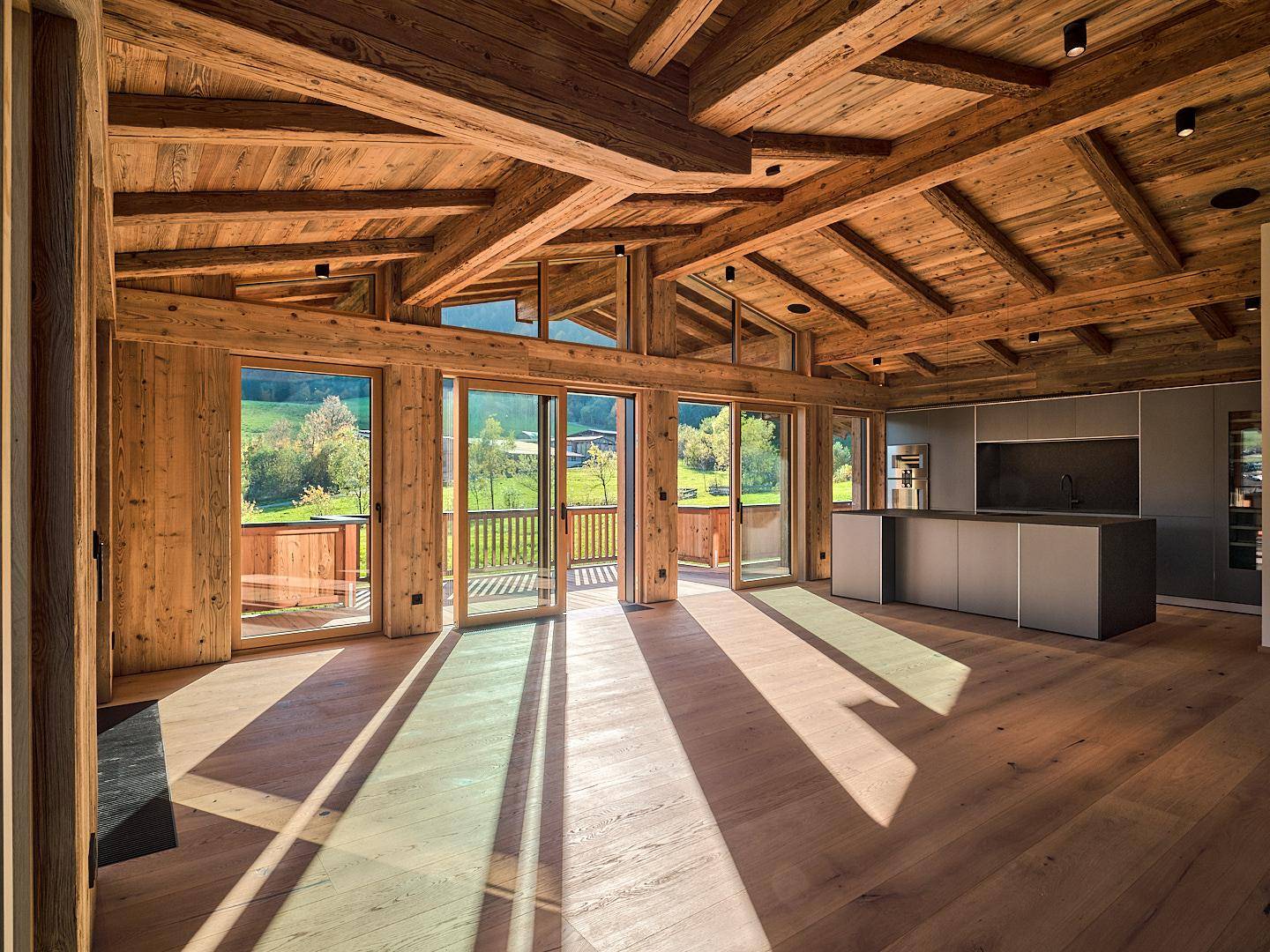 Offener Wohnbereich mit moderner Küche, Holzbalken und Zugang zum Balkon mit Aussicht.