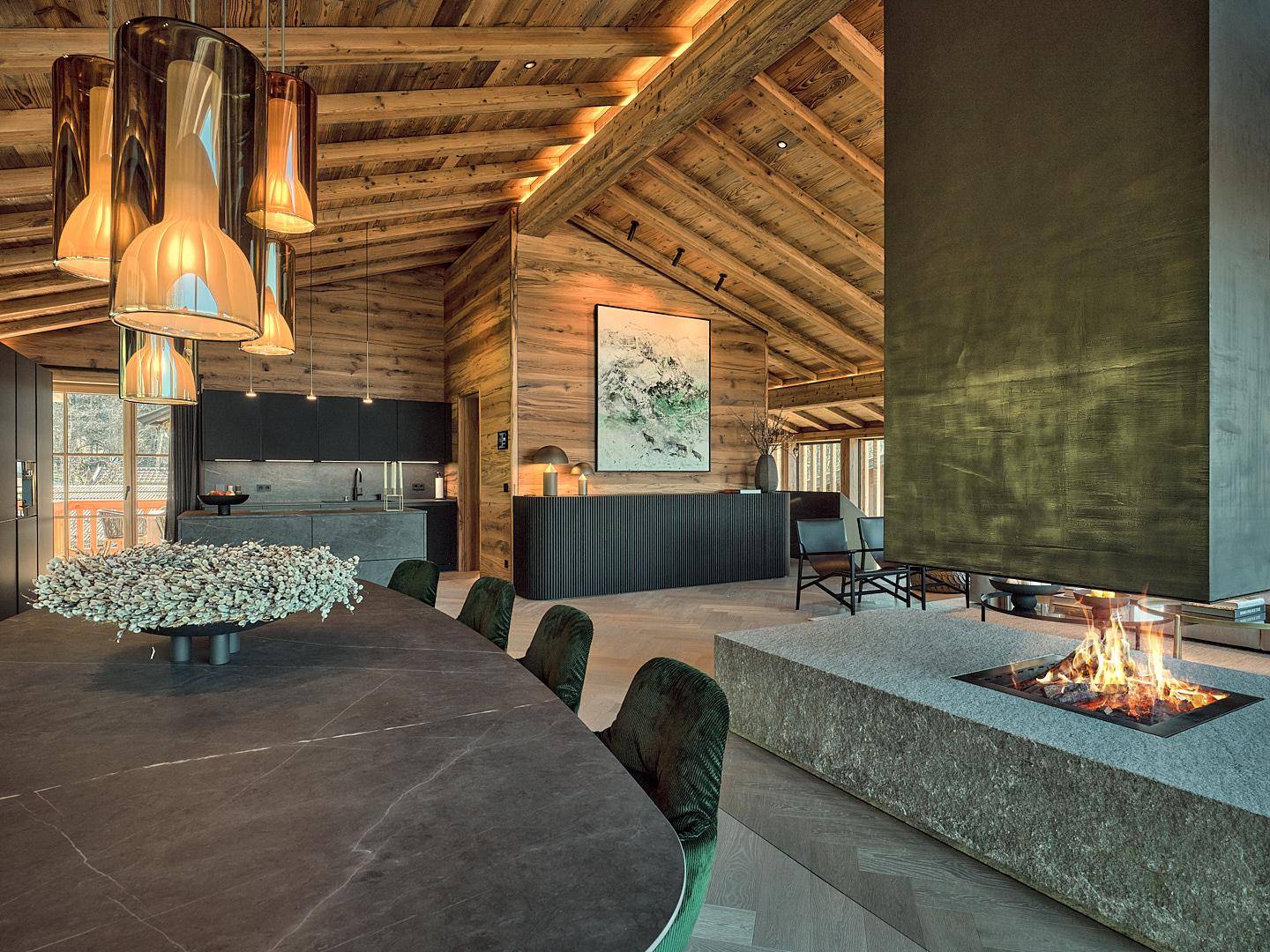 Eleganter Essbereich mit moderner Küche im Hintergrund, Holzbalkendecke und integriertem Kamin.