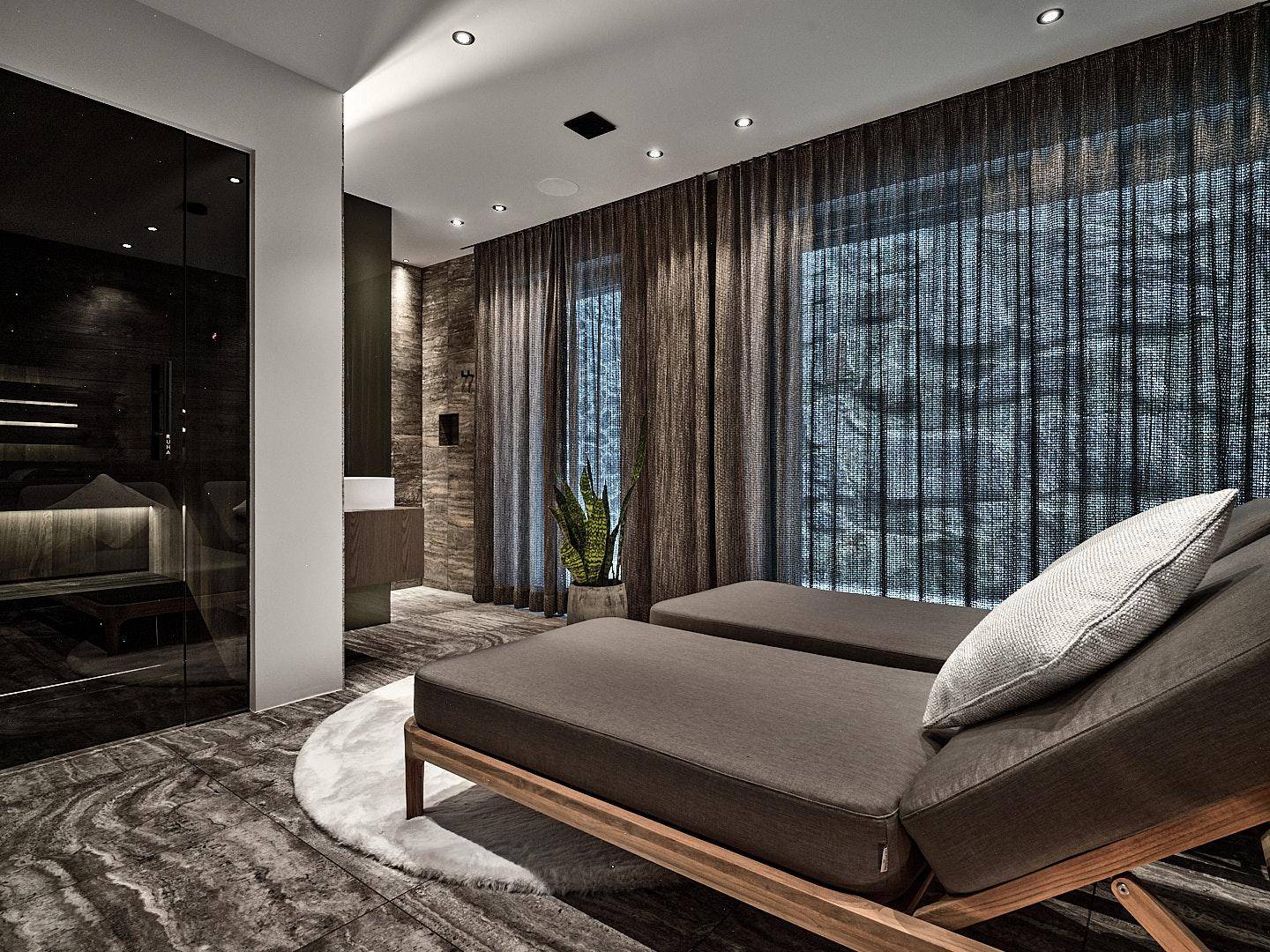 Moderner Wellnessbereich mit Liegen, dunklen Vorhängen und einer sichtbaren Sauna im Hintergrund.