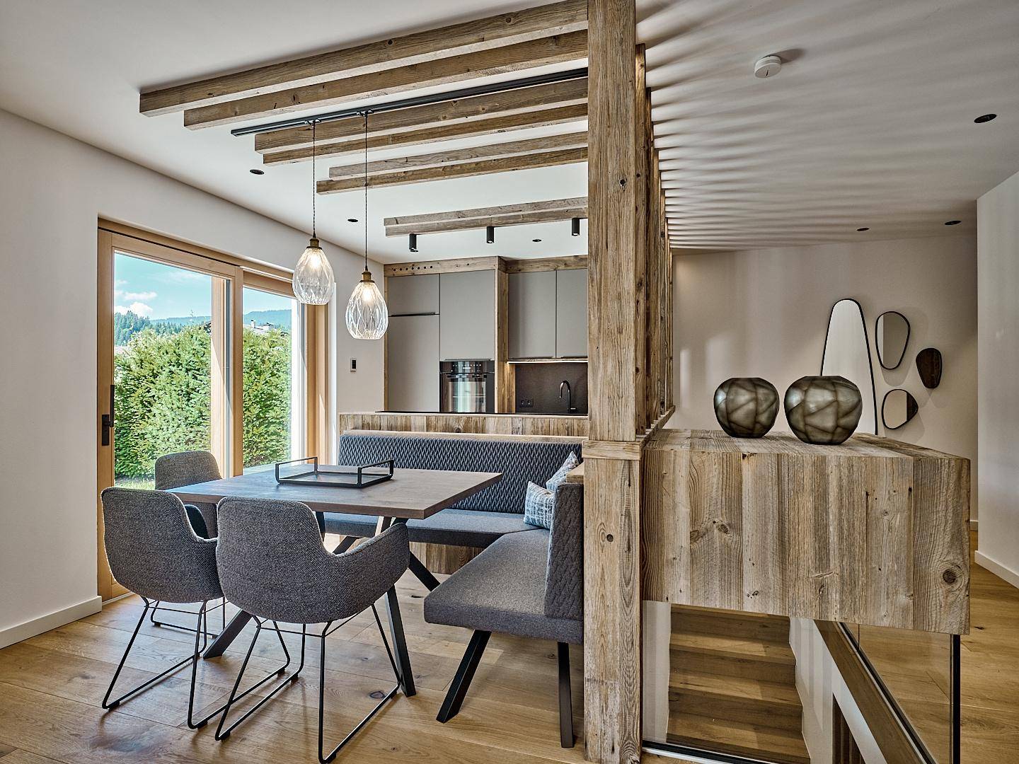Moderner Essbereich mit Holzbalken, integrierter Sitzbank und offener Küche im Hintergrund.