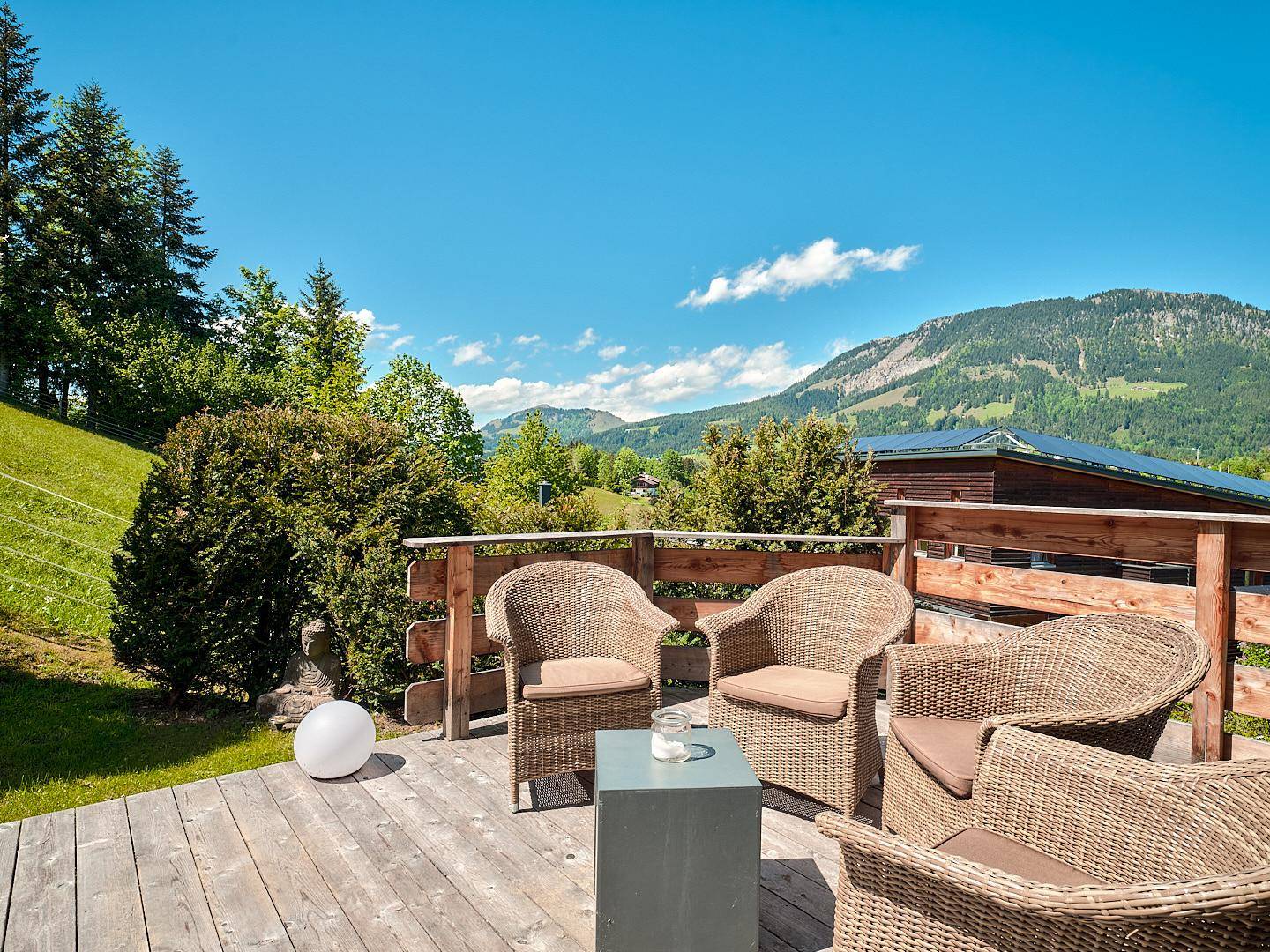 Sonnige Holzterrasse mit bequemen Korbmöbeln und einem weiten Blick auf die umliegende Berglandschaft.