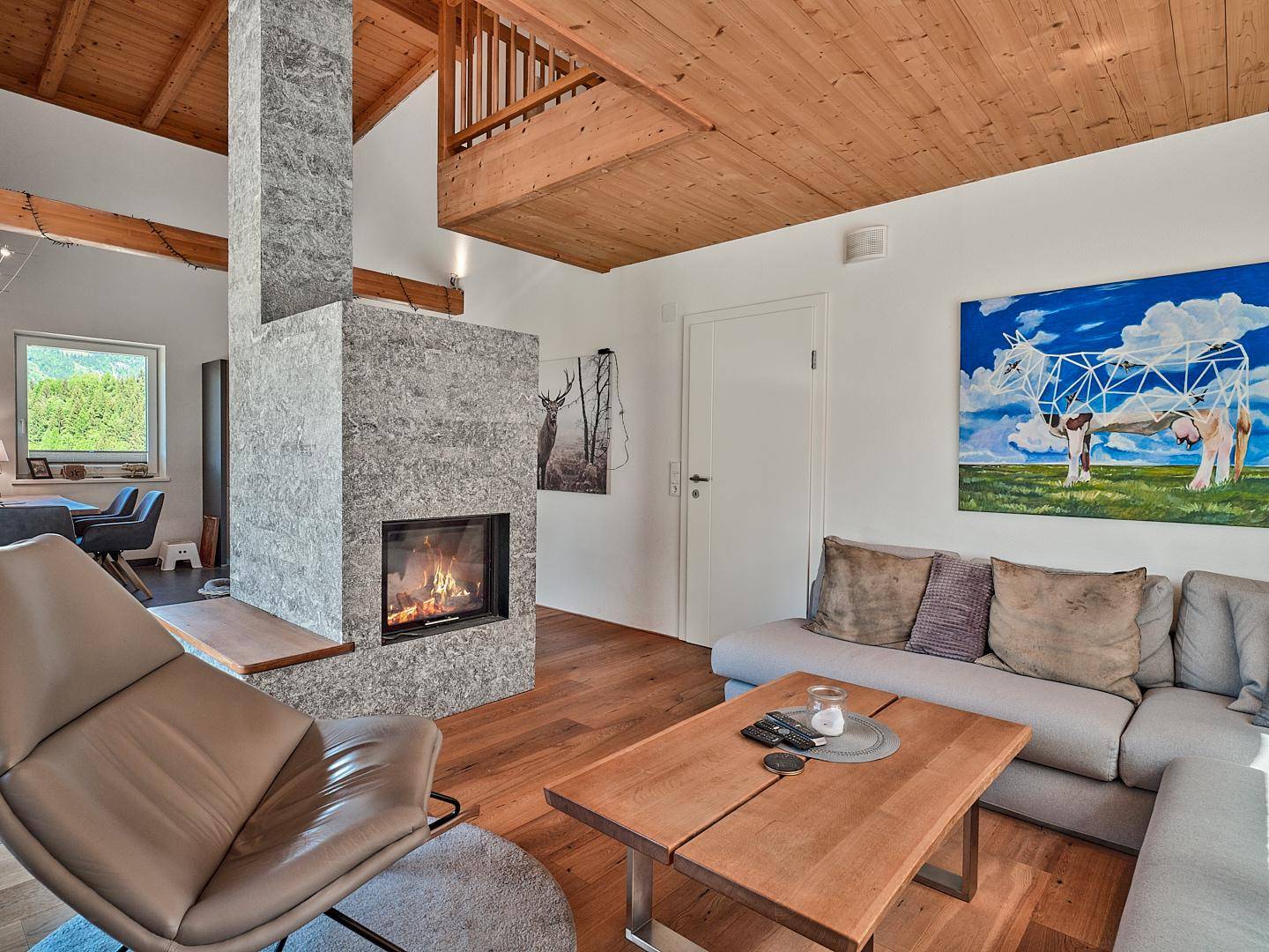 Gemütliches Wohnzimmer mit modernem Kamin, Holzbalkendecke und einem farbenfrohen Kunstwerk an der Wand.