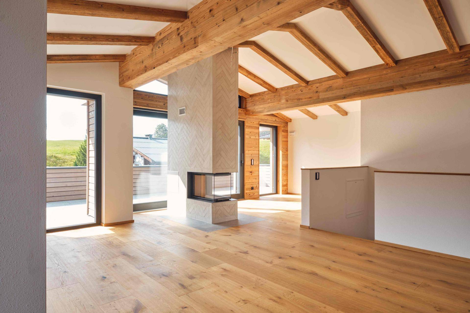 Heller, offener Wohnbereich mit beeindruckenden Holzbalken, modernem Kamin und Zugang zur Terrasse.