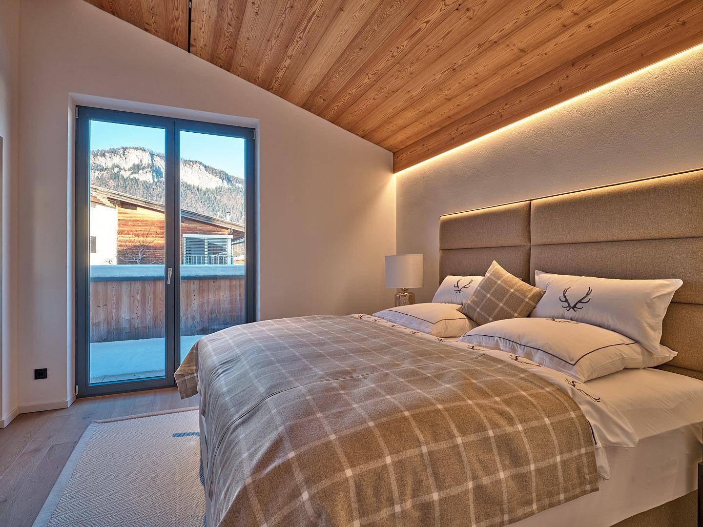 Gemütliches Schlafzimmer mit Holzbalkendecke, gepolstertem Kopfteil und Bergblick.