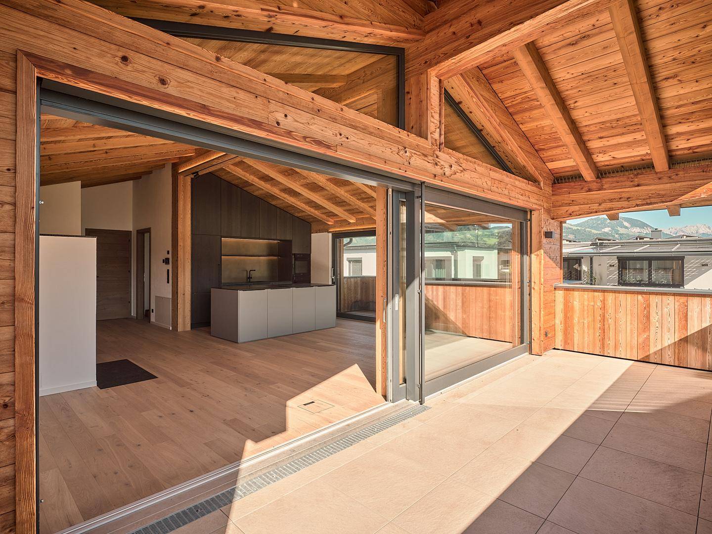 Heller Innenraum mit Holzbalkendecke und Zugang zu einer großzügigen überdachten Terrasse.
