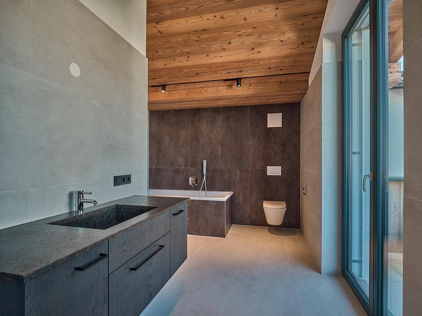 Modernes Badezimmer mit dunklem Waschtisch, Badewanne und Holzbalkendecke.