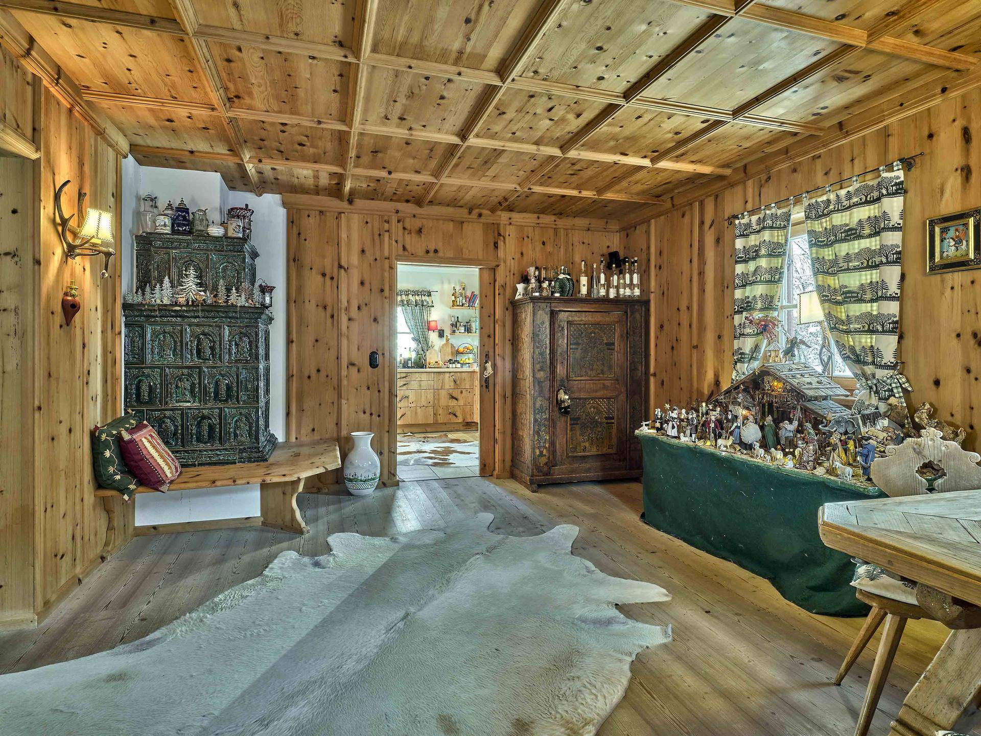 Gemütliches Wohnzimmer im alpenländischen Stil mit Holztäfelung, Kachelofen und traditioneller Dekoration.