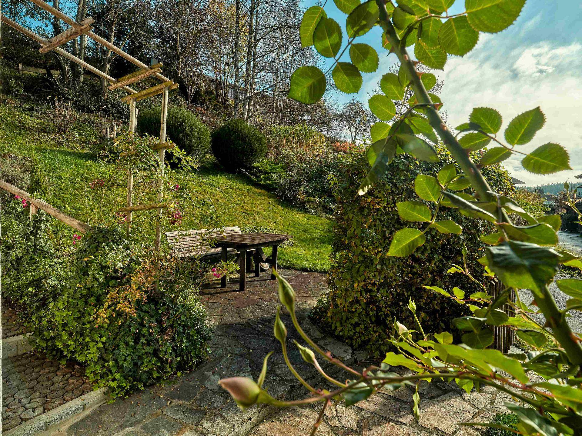 Idyllischer Gartenbereich mit Sitzgelegenheiten, Rasenfläche und Blick auf die grüne Hügellandschaft.