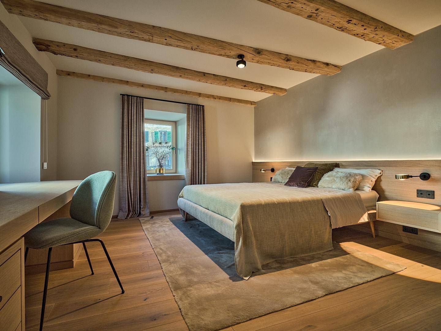 Gemütliches Schlafzimmer mit Holzbalken an der Decke, Holzboden und Schreibtischbereich.