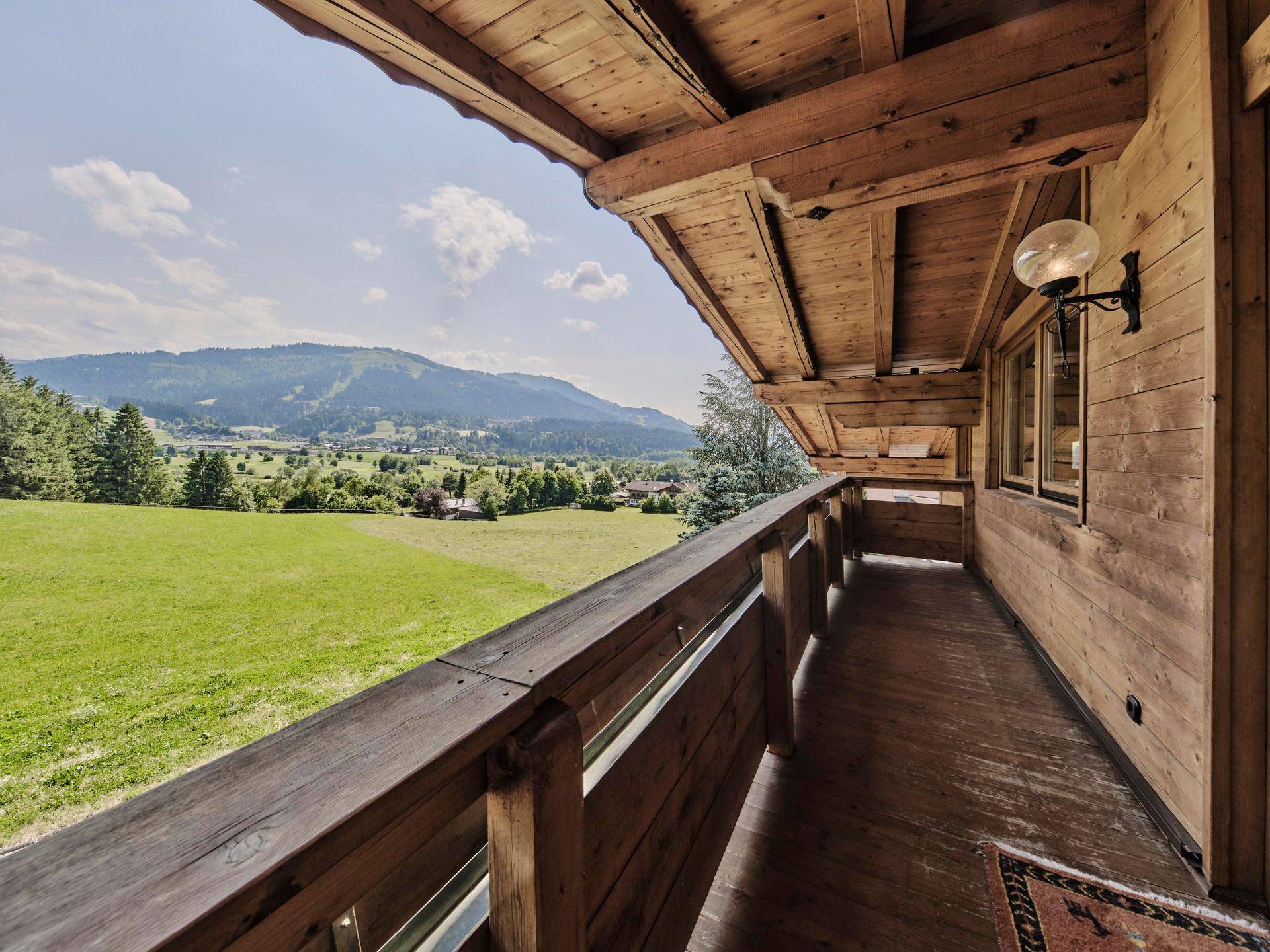 Traditioneller Holzbalkon mit weitem Blick über grüne Wiesen und die umliegende Berglandschaft.