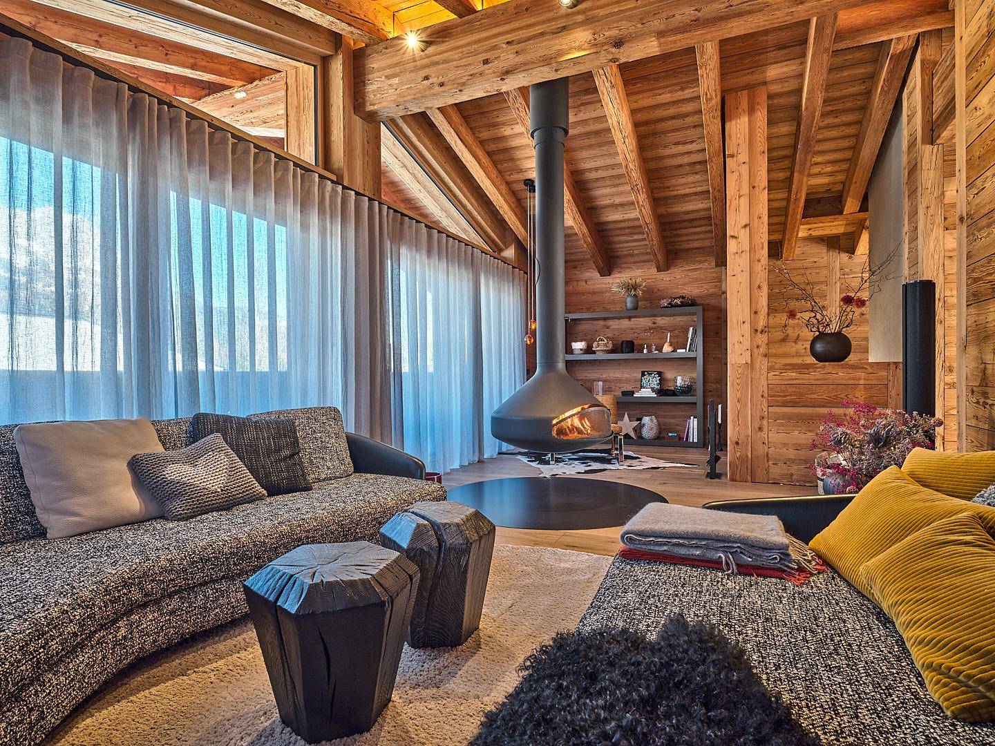 Gemütliches Wohnzimmer im alpinen Stil mit Holzbalkendecke und modernem Hängekamin.