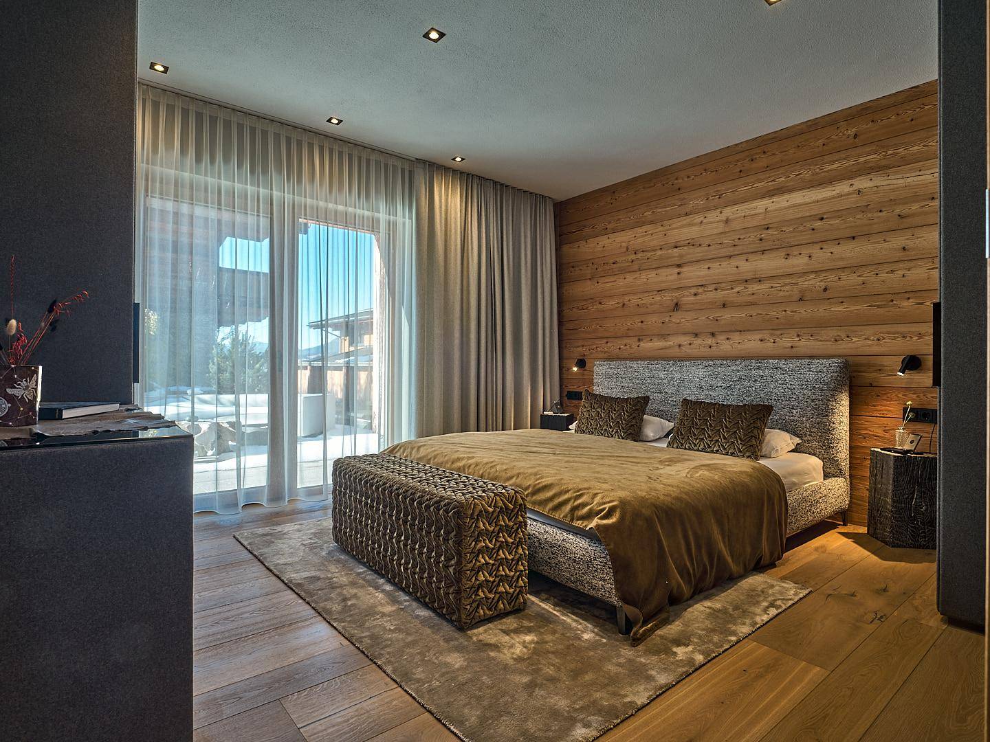 Helles Schlafzimmer mit Holzwand, großem Bett und direktem Zugang zur Terrasse.