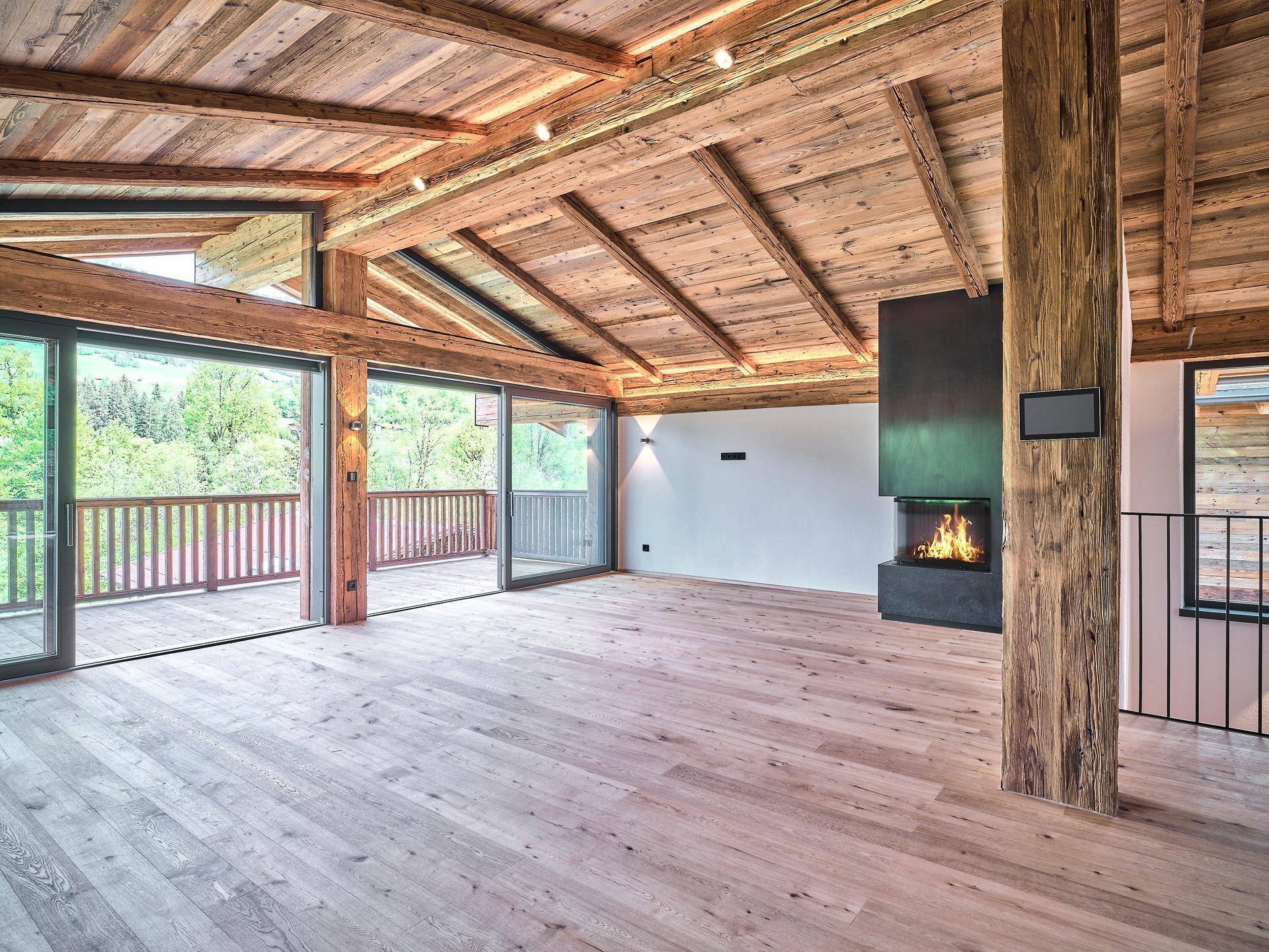 Geräumiges Wohnzimmer mit Holzbalkendecke, modernem Kamin und Zugang zu einem großen Balkon.