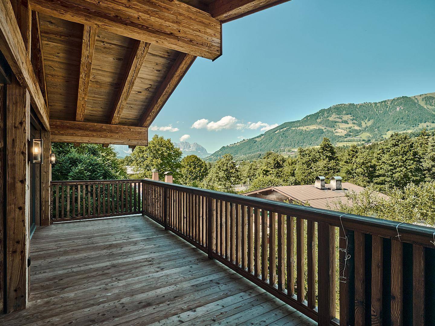 Großer Holzbalkon mit Panoramablick auf die umliegende Berglandschaft und viel Grün.