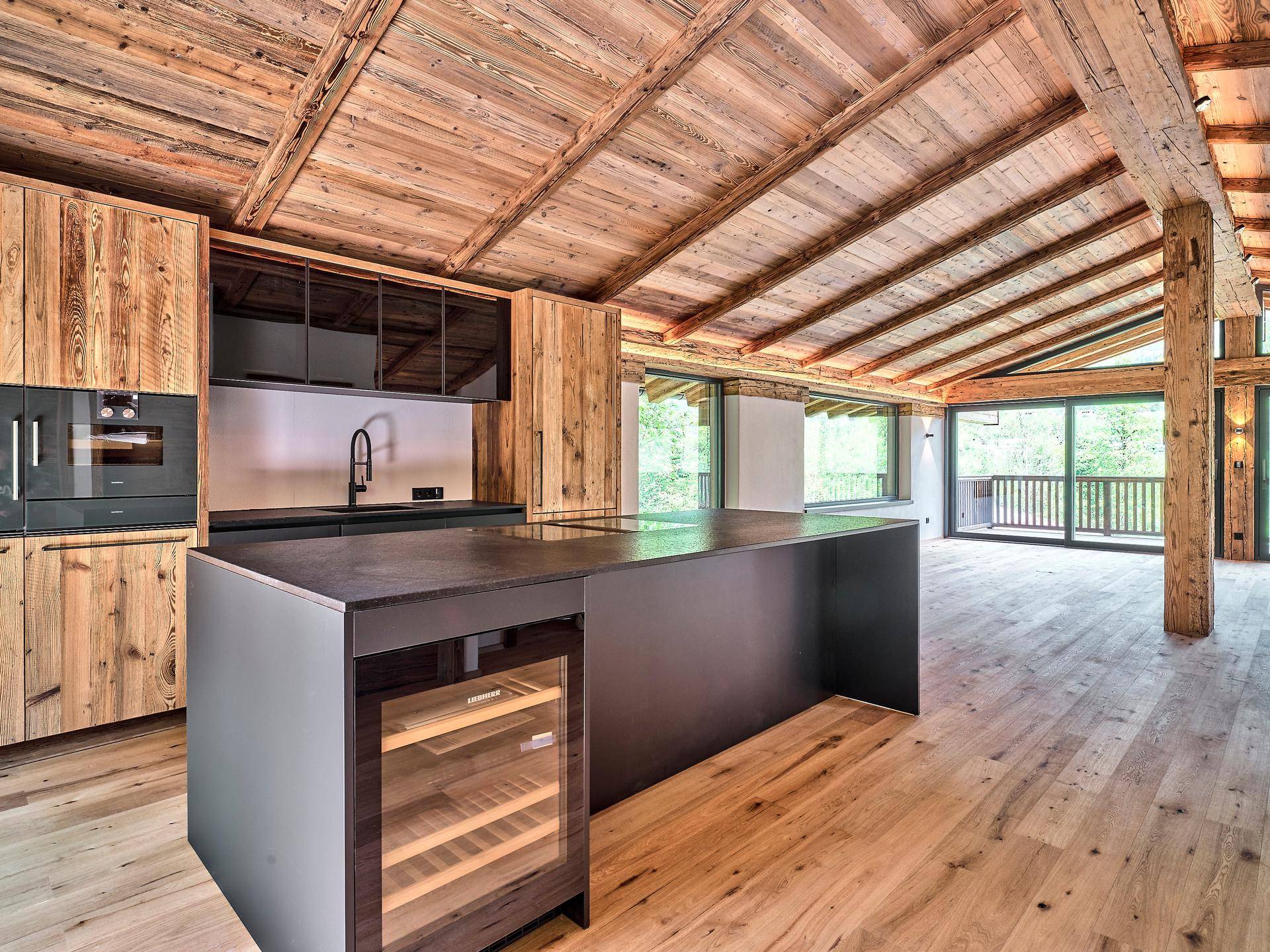 Moderne Küche mit dunkler Kücheninsel, integrierten Geräten und rustikalen Holzdecken.