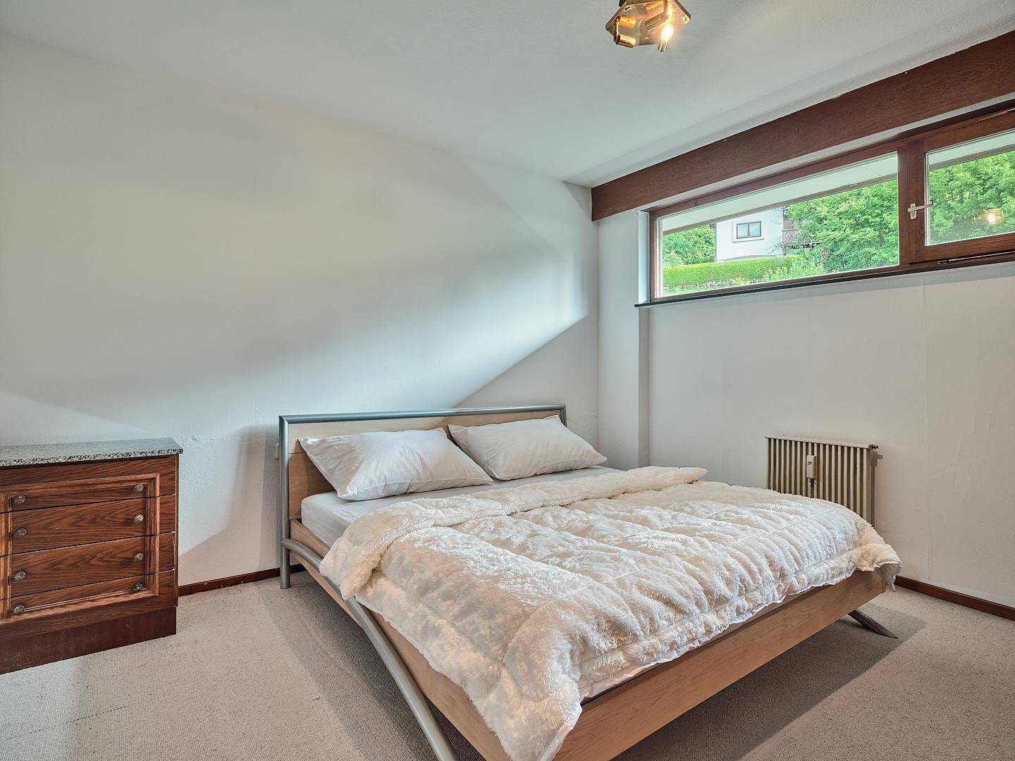Gemütliches Schlafzimmer mit Doppelbett und Heizkörper, mit Blick ins Grüne durch das Fenster.