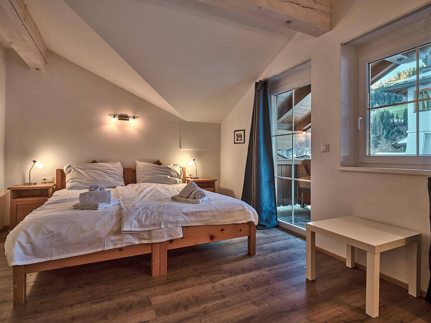 Gemütliches Schlafzimmer mit Doppelbett, Holzbalken und Zugang zu einem Balkon mit Bergblick.