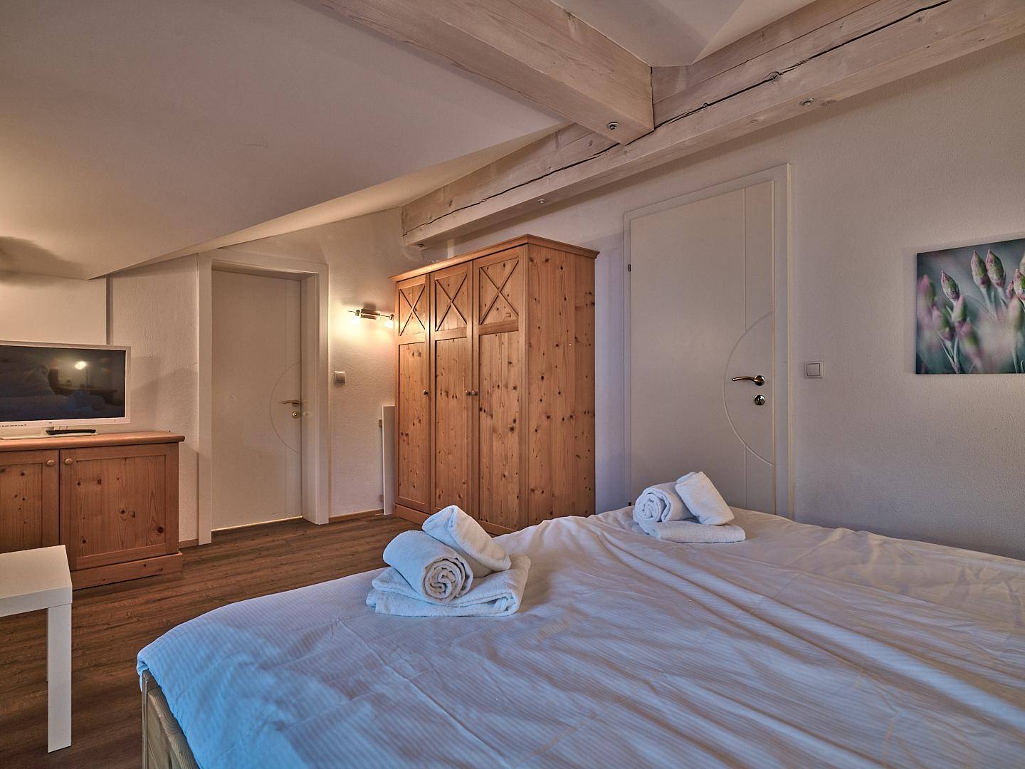 Schlafzimmer mit Holzbett, großem Kleiderschrank und Fernseher unter sichtbaren Holzbalken.