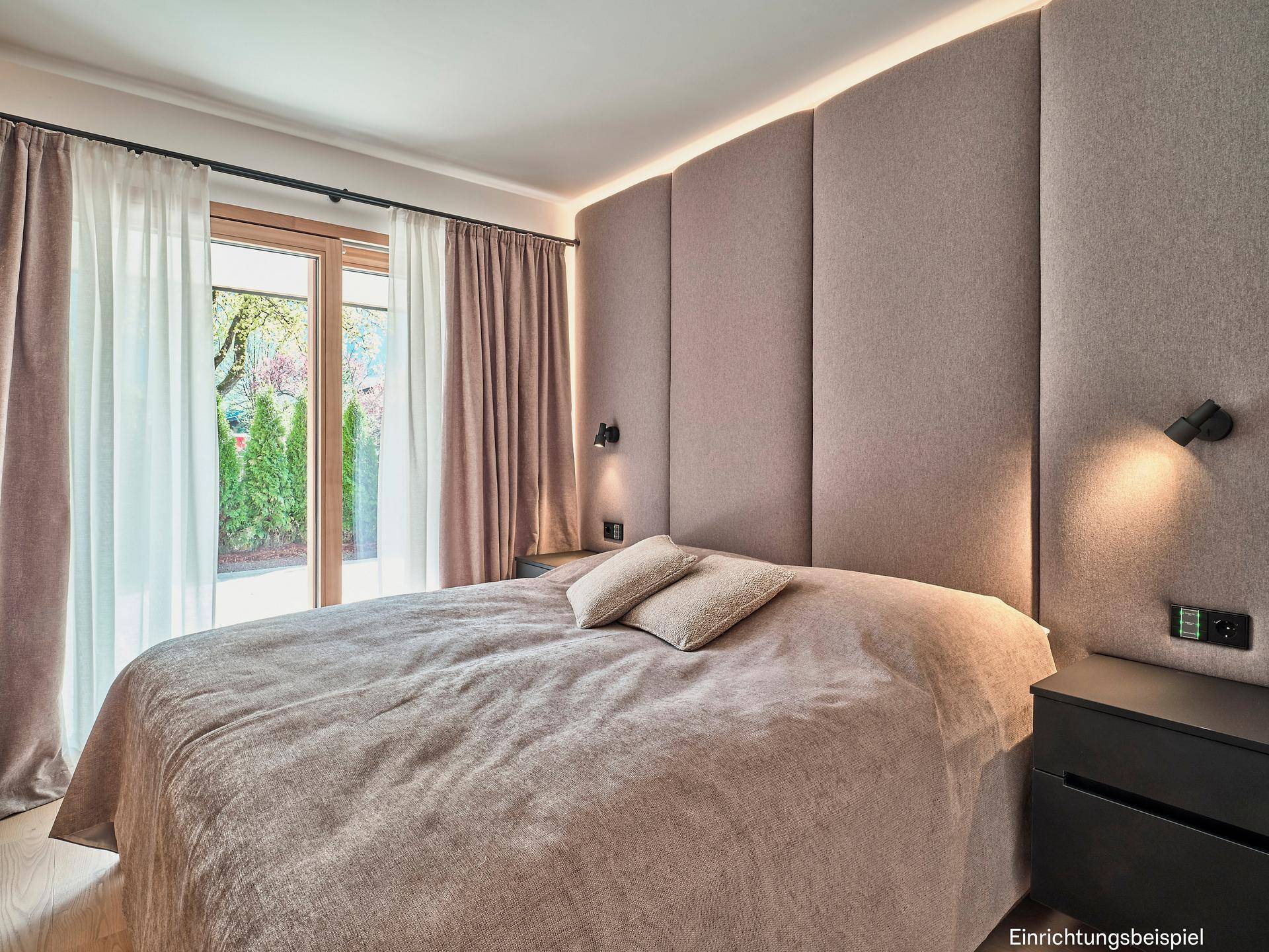 Helles Schlafzimmer mit großem Bett, gepolstertem Kopfteil und Zugang zu einem Außenbereich mit viel Grün.