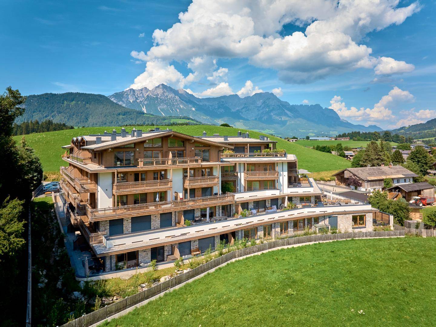 Moderne Wohnanlage in alpiner Landschaft mit zahlreichen Balkonen und beeindruckendem Bergblick unter blauem Himmel.