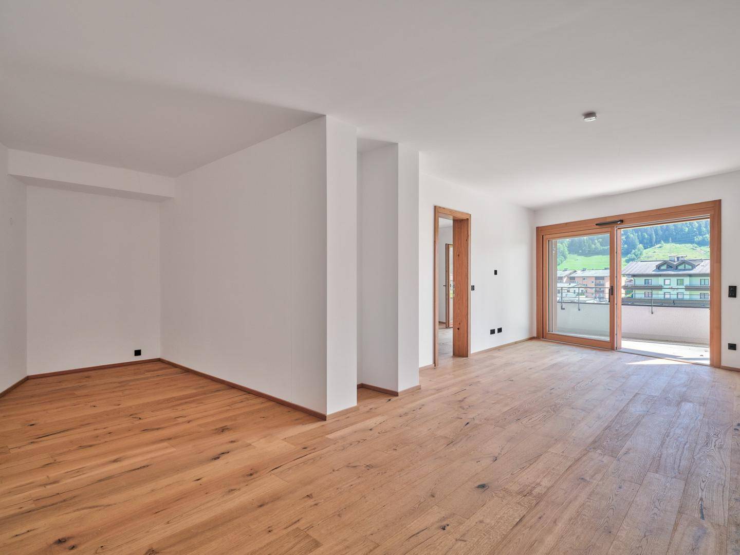 Heller, unmöblierter Wohnbereich mit Eichenparkett und großem Schiebefenster zum Balkon mit Bergblick.